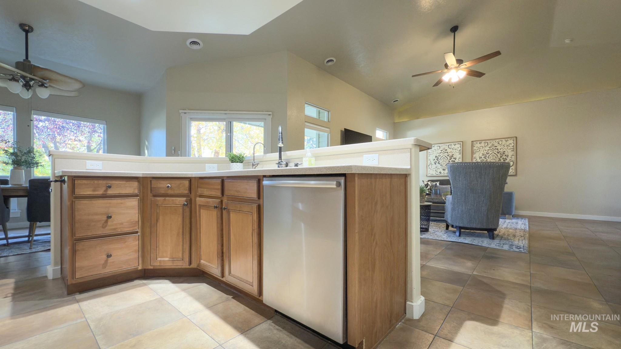 Kitchen featuring ceiling fan, brown cabinetry, vaulted ceiling, stainless steel dishwasher, and light countertops