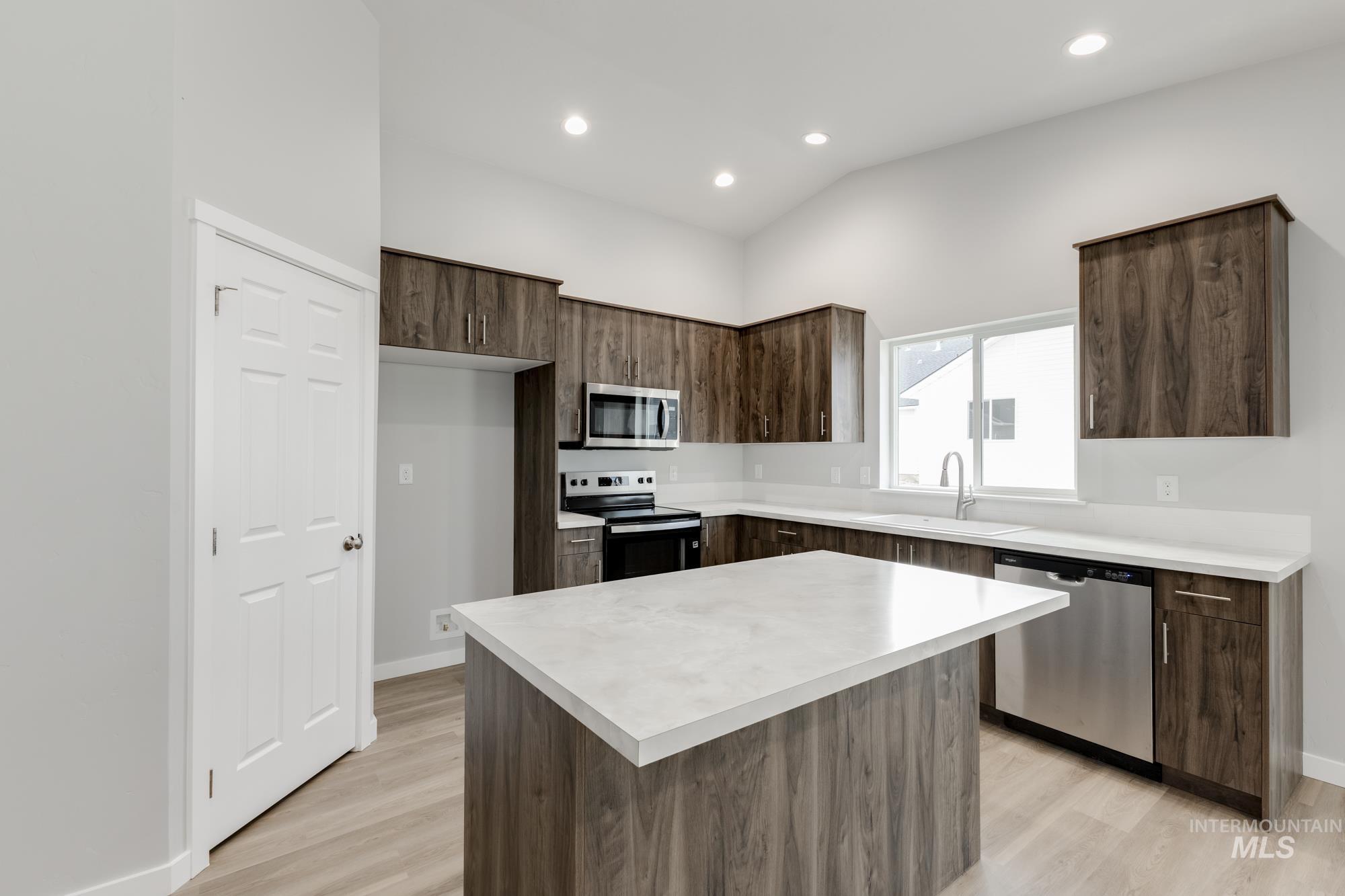 Kitchen featuring dark brown cabinetry, modern cabinets, light countertops, stainless steel appliances, and a kitchen island