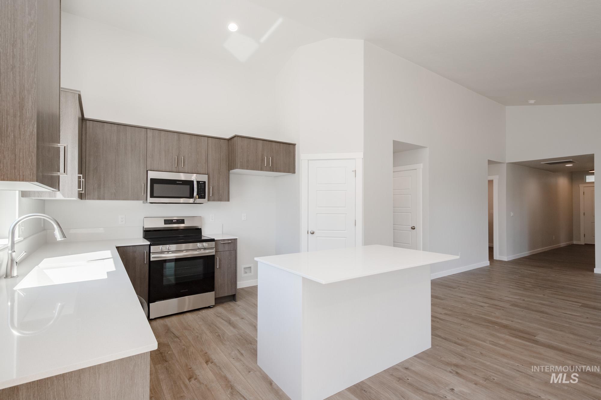 Kitchen with high vaulted ceiling, stainless steel appliances, a kitchen island, modern cabinets, and light wood-style flooring