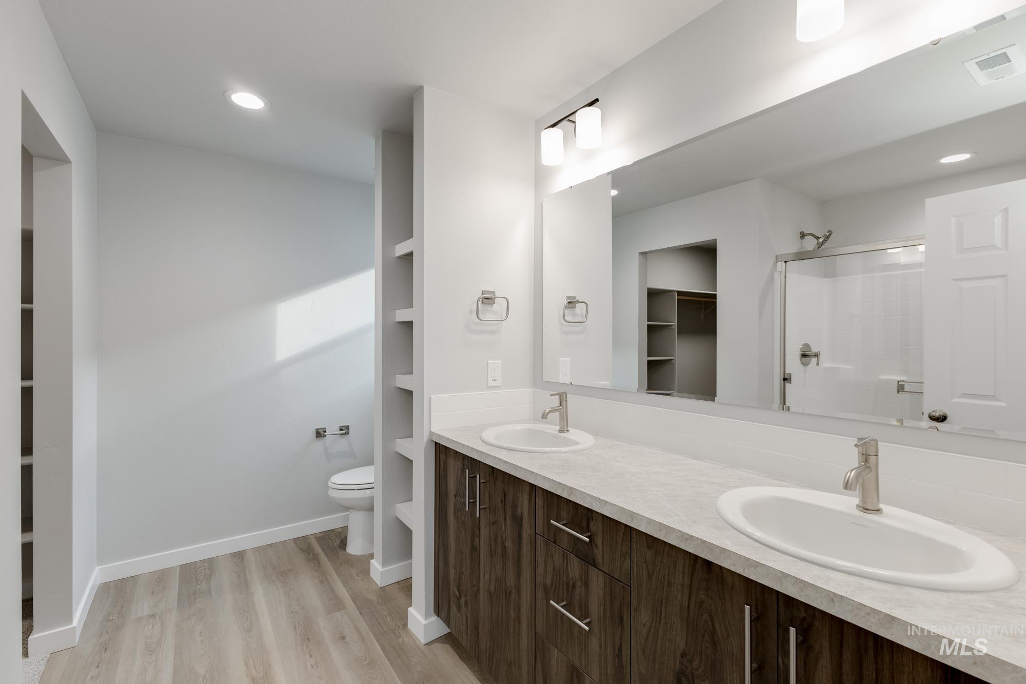 Full bathroom with a walk in closet, a stall shower, double vanity, light wood-style flooring, and recessed lighting