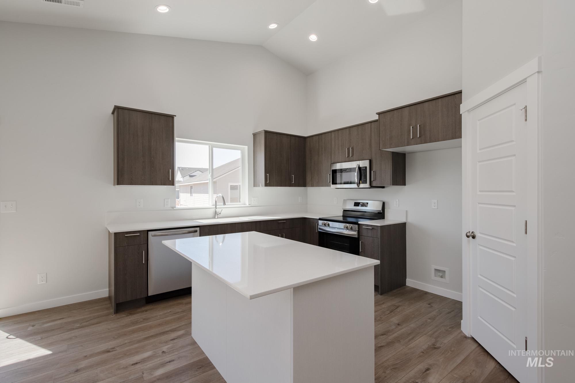 Kitchen featuring dark brown cabinets, appliances with stainless steel finishes, high vaulted ceiling, light wood finished floors, and modern cabinets