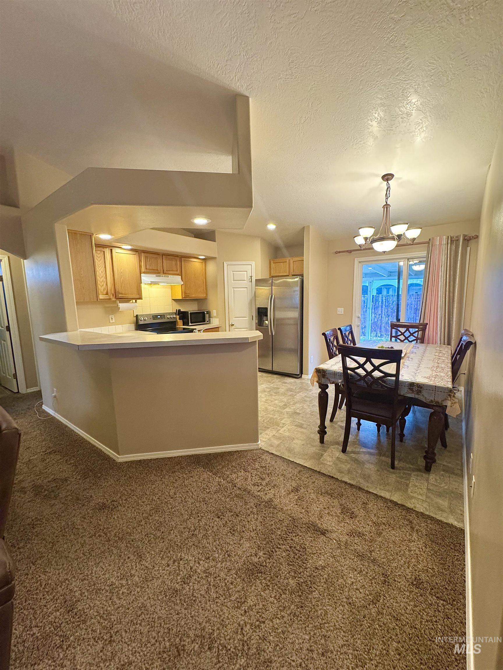 Kitchen with light colored carpet, a peninsula, hanging lights, stainless steel appliances, and light countertops
