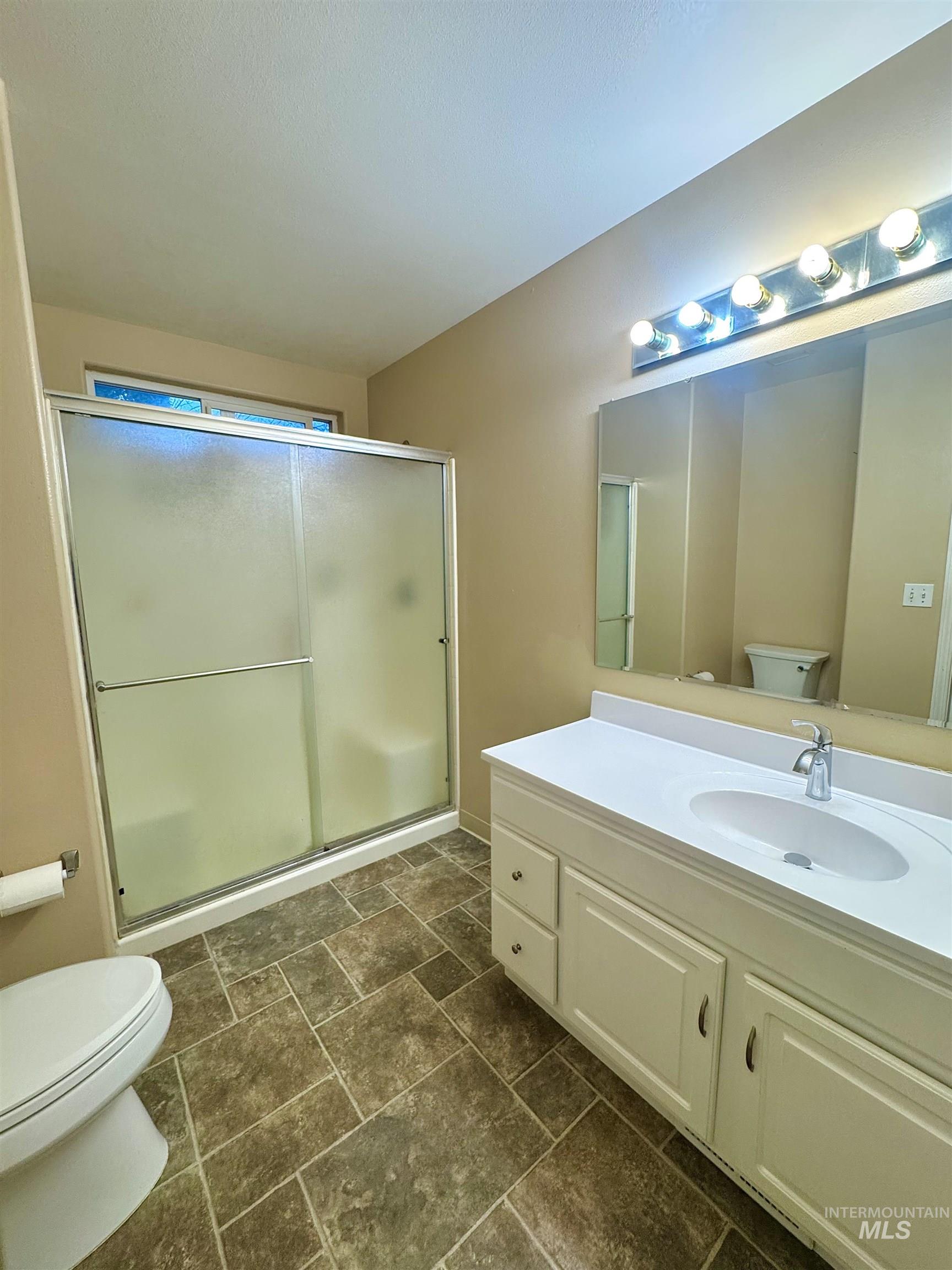 Bathroom featuring a stall shower, vanity, and dark stone finish flooring