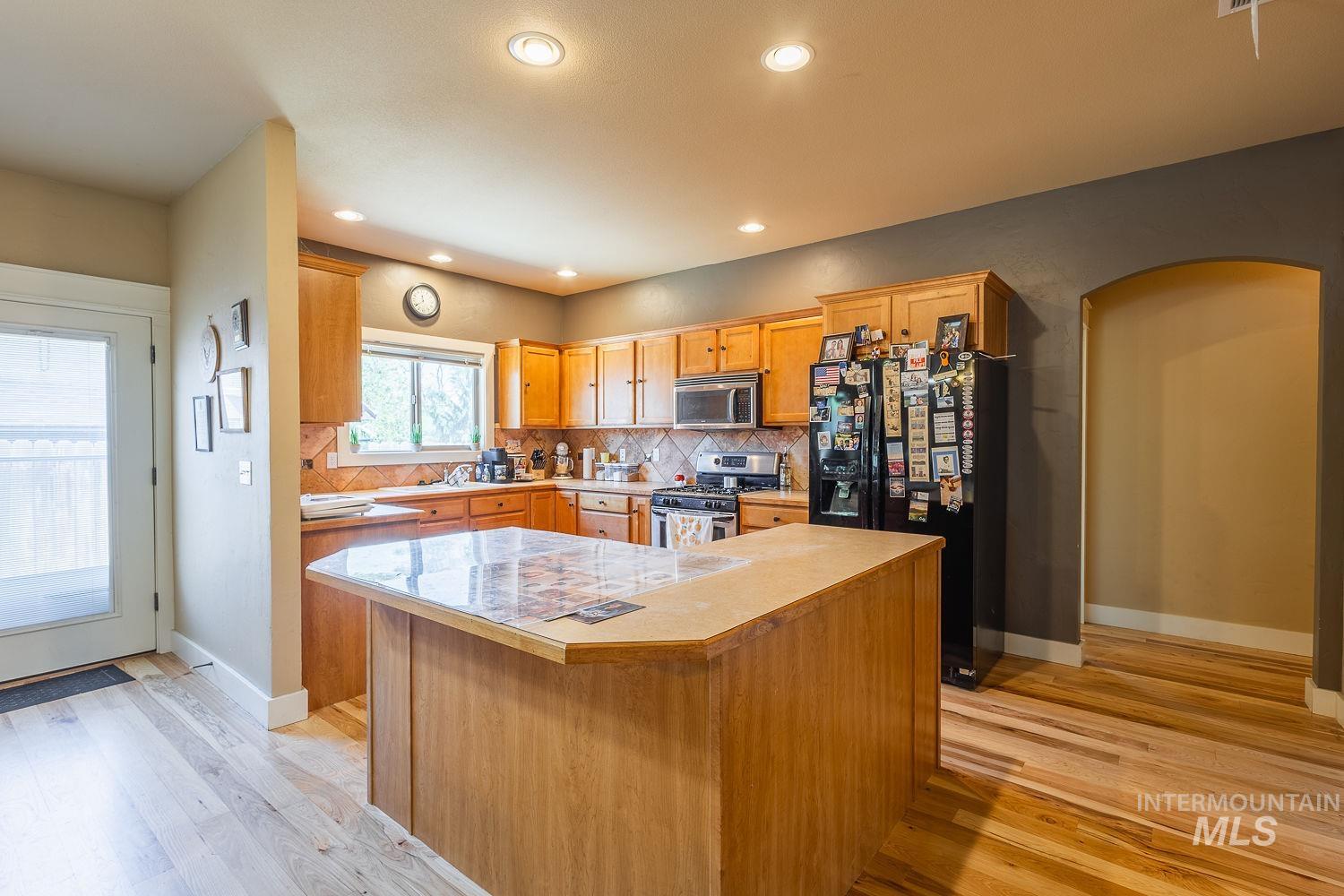 Kitchen featuring stainless steel appliances, tasteful backsplash, light wood-type flooring, light countertops, and arched walkways