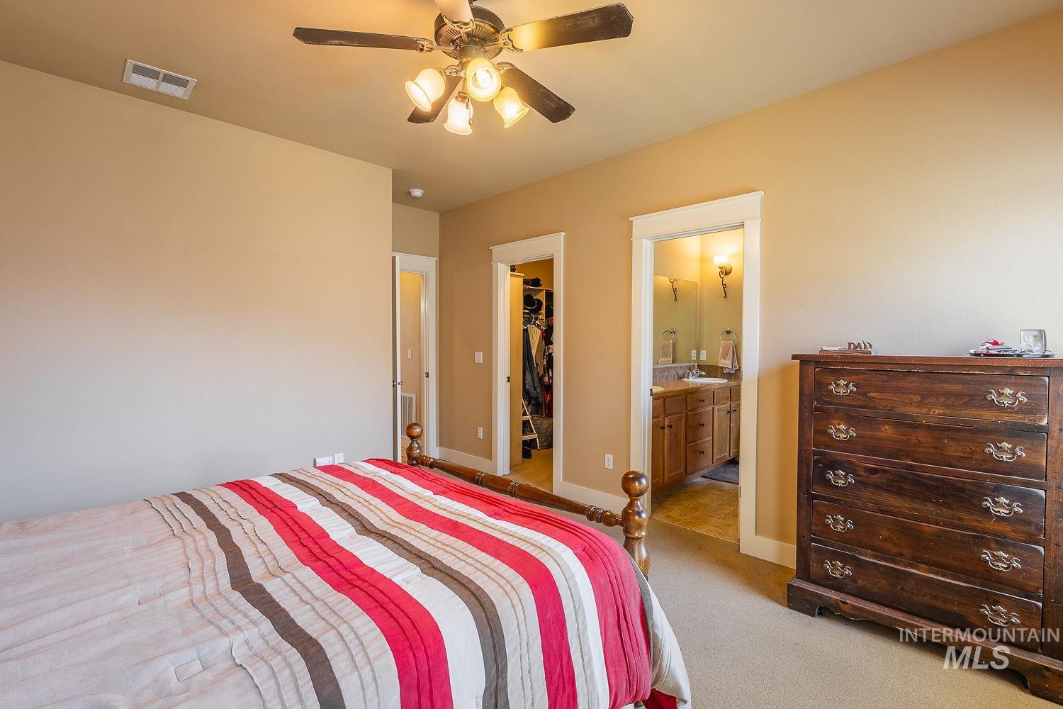 Carpeted bedroom featuring a walk in closet, ensuite bath, and ceiling fan