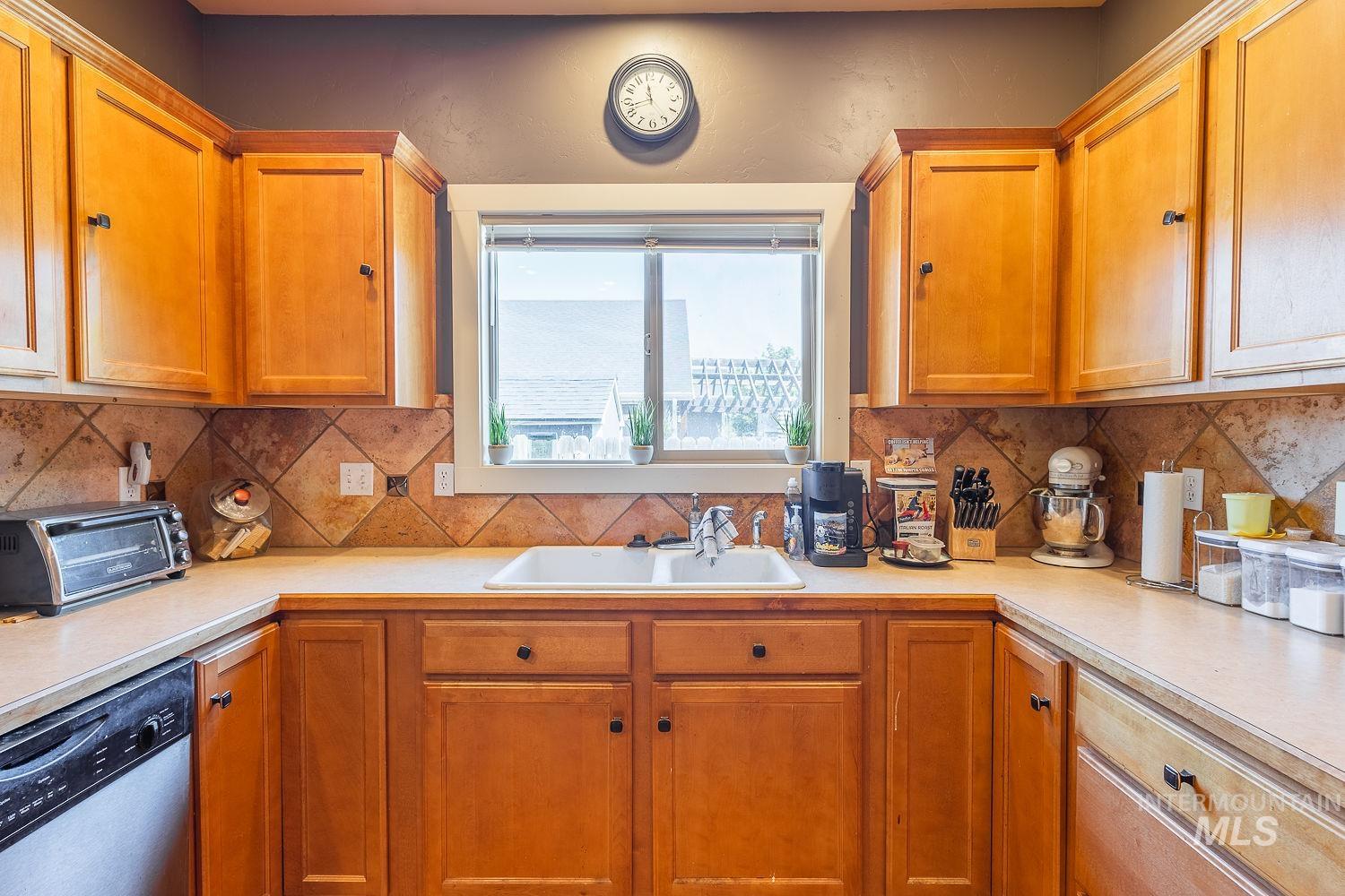 Kitchen with stainless steel dishwasher, light countertops, and brown cabinets