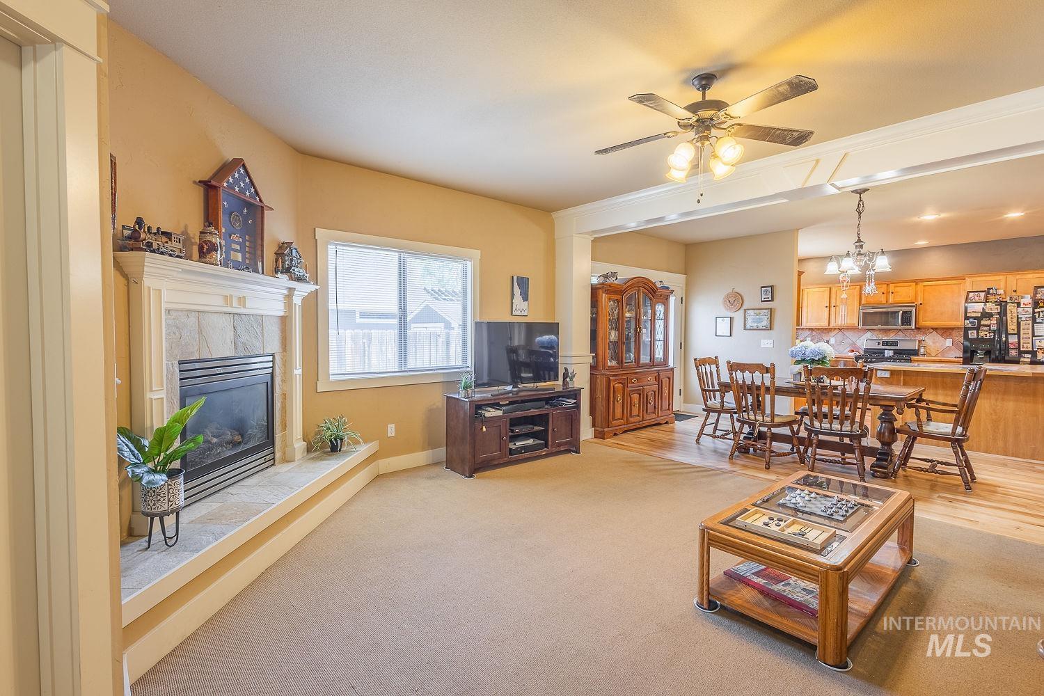 Living room featuring a fireplace, a ceiling fan, light carpet, and a chandelier