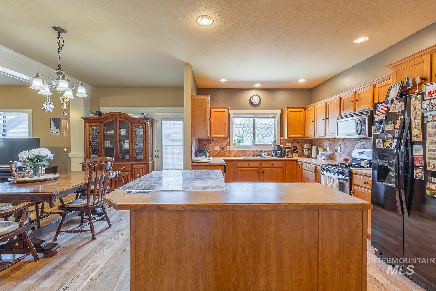 Kitchen with backsplash, appliances with stainless steel finishes, light wood-style floors, a chandelier, and decorative light fixtures