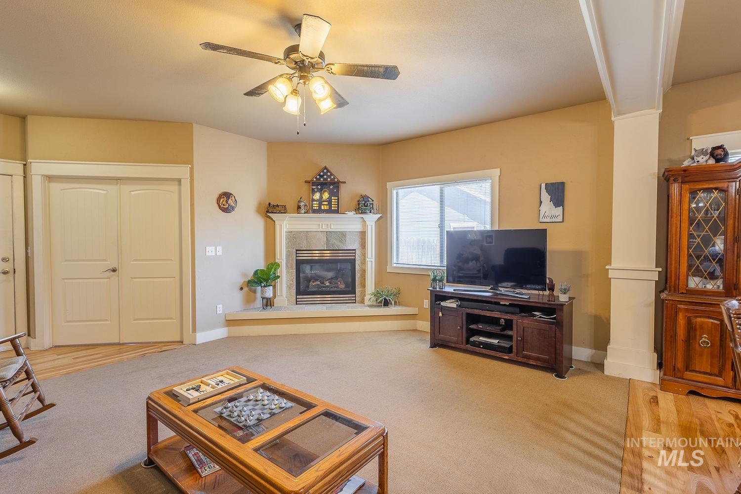 Carpeted living room featuring decorative columns, a tiled fireplace, and ceiling fan