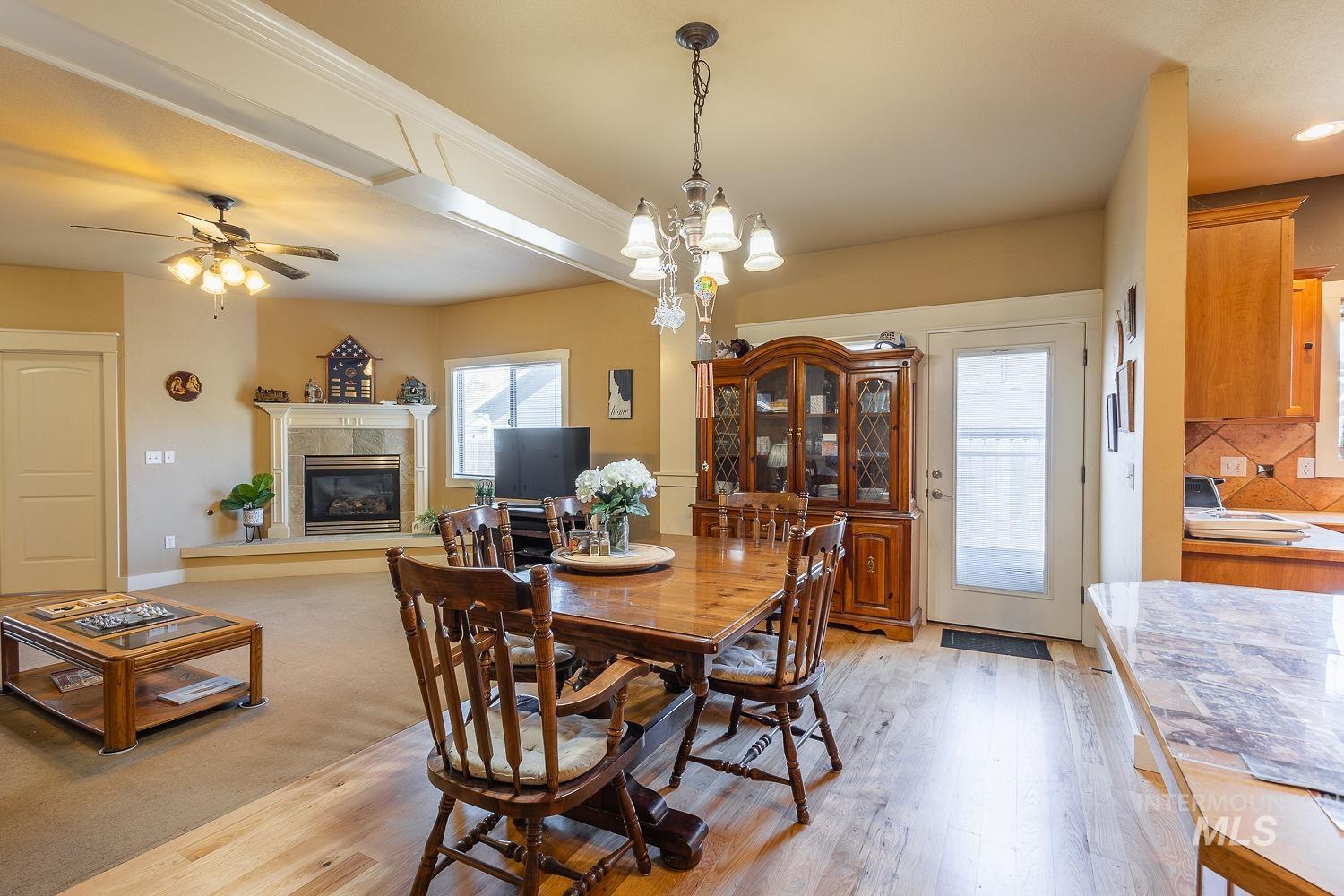 Dining area with a tile fireplace, light wood finished floors, a ceiling fan, and a chandelier
