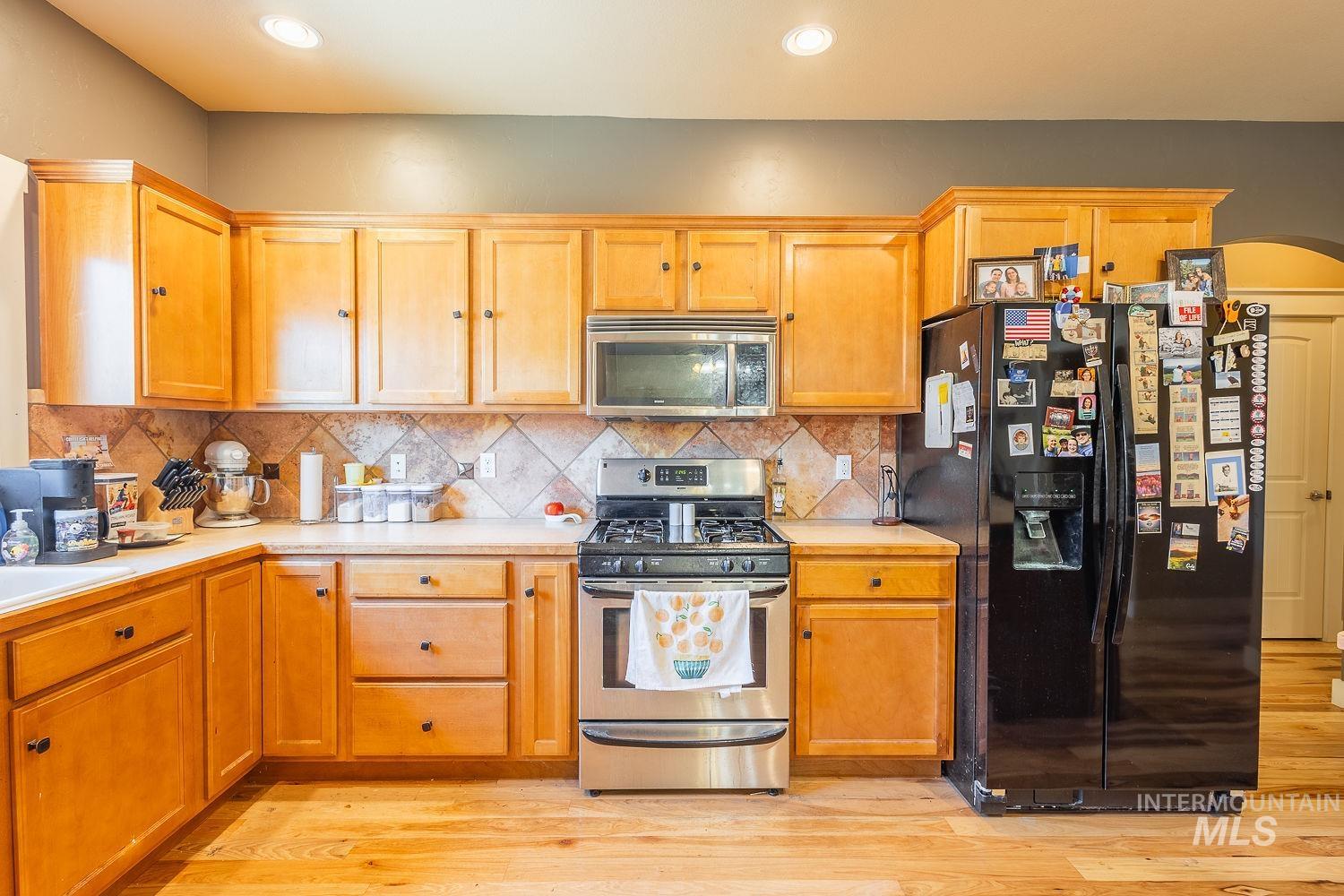 Kitchen with appliances with stainless steel finishes, light countertops, decorative backsplash, arched walkways, and recessed lighting