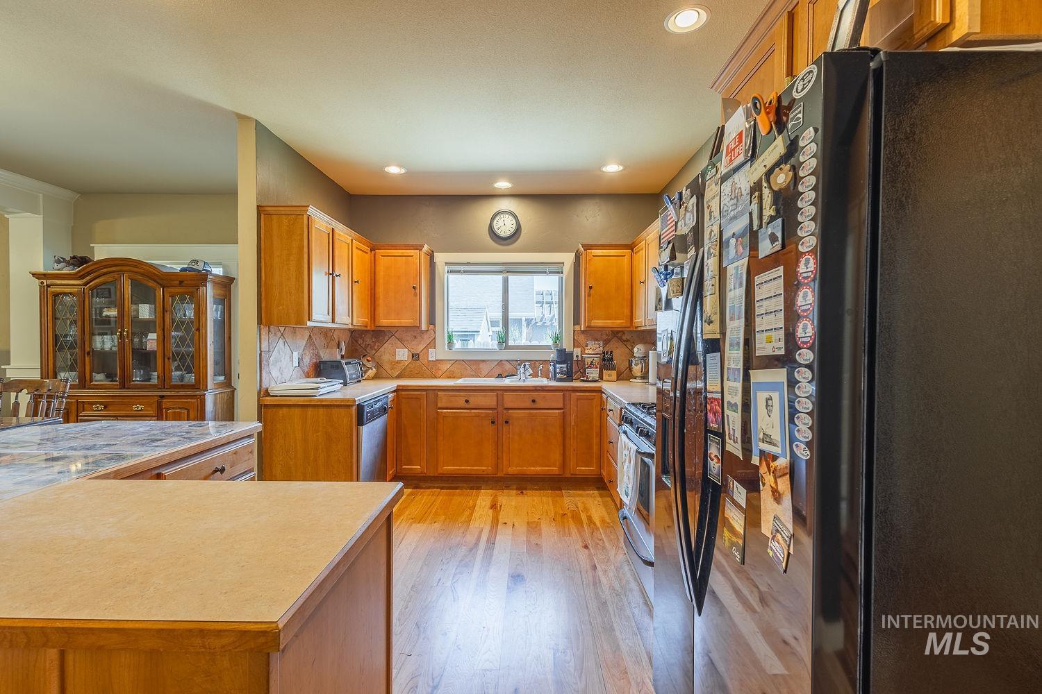 Kitchen with stainless steel appliances, tasteful backsplash, brown cabinets, light wood-style floors, and light countertops