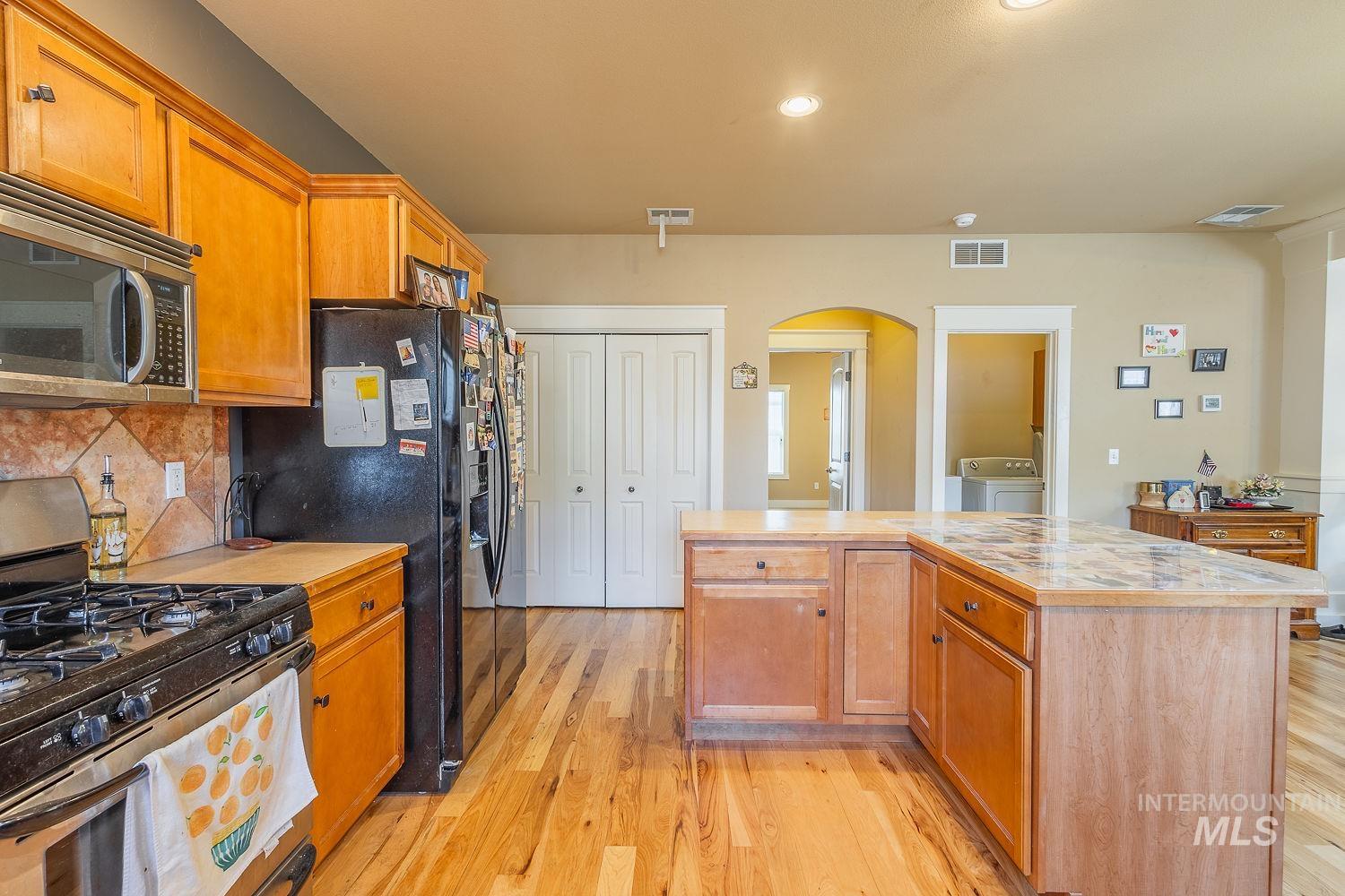 Kitchen with stainless steel appliances, arched walkways, light countertops, light wood-style flooring, and a kitchen island