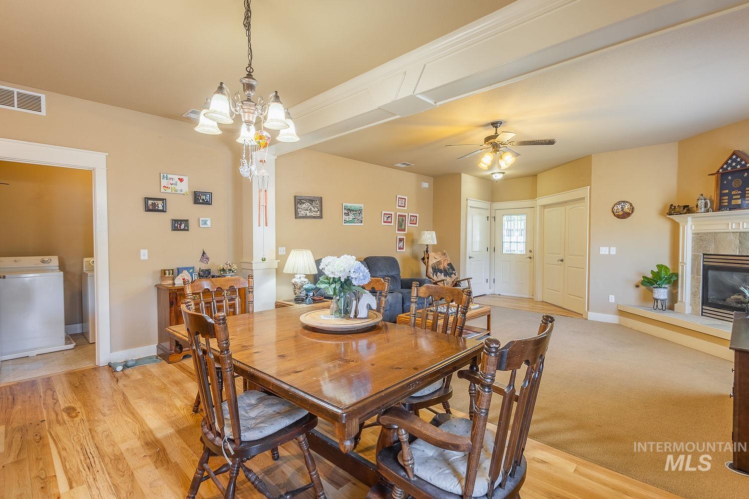 Dining space featuring washer / dryer, light wood-style flooring, a ceiling fan, a tiled fireplace, and a chandelier