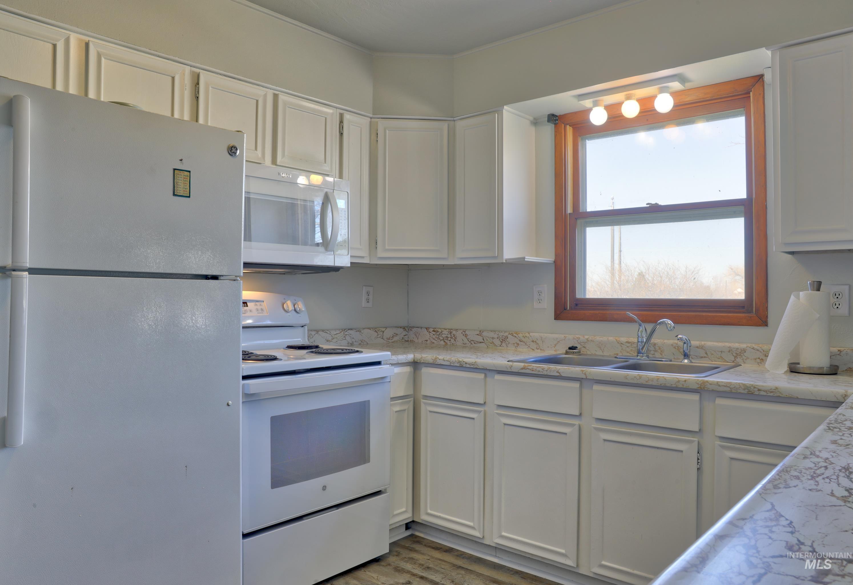 Kitchen featuring white appliances, white cabinetry, light countertops, and light wood finished floors