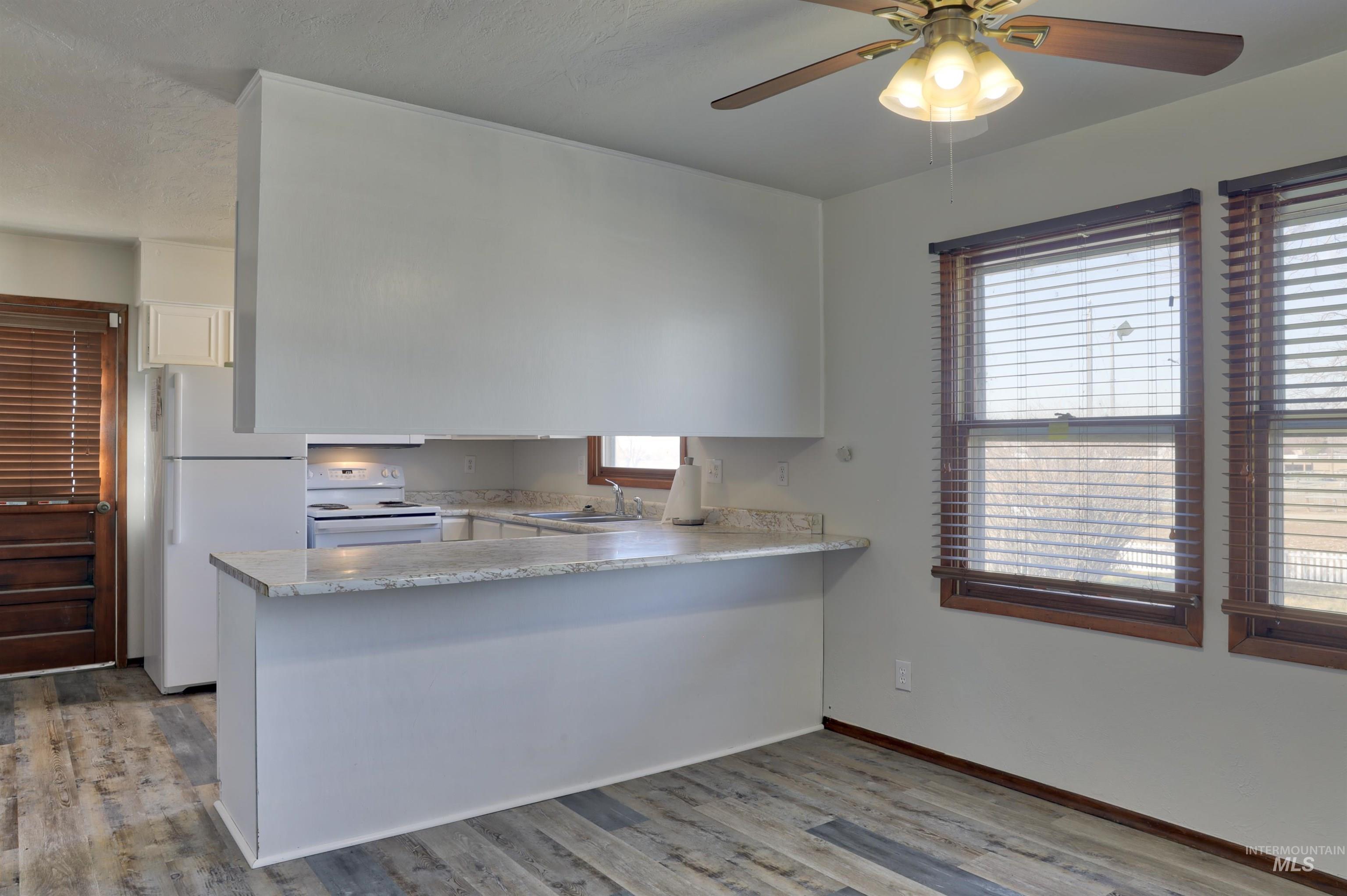 Kitchen with white appliances, light wood-type flooring, a ceiling fan, a peninsula, and white cabinetry