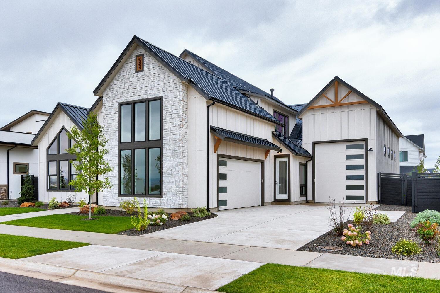 Modern farmhouse style home with a metal roof, stone siding, a standing seam roof, driveway, and an attached garage
