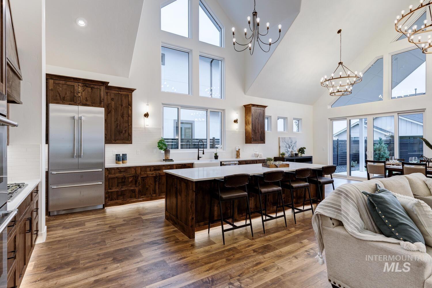 Kitchen with tasteful backsplash, open floor plan, dark brown cabinets, stainless steel built in refrigerator, and high vaulted ceiling