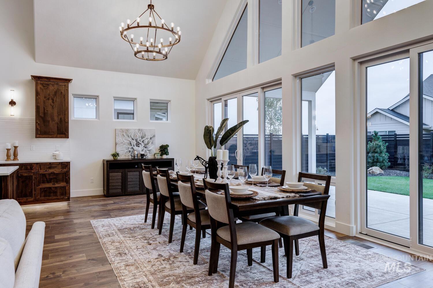 Dining area with high vaulted ceiling, plenty of natural light, dark wood-style floors, and a chandelier