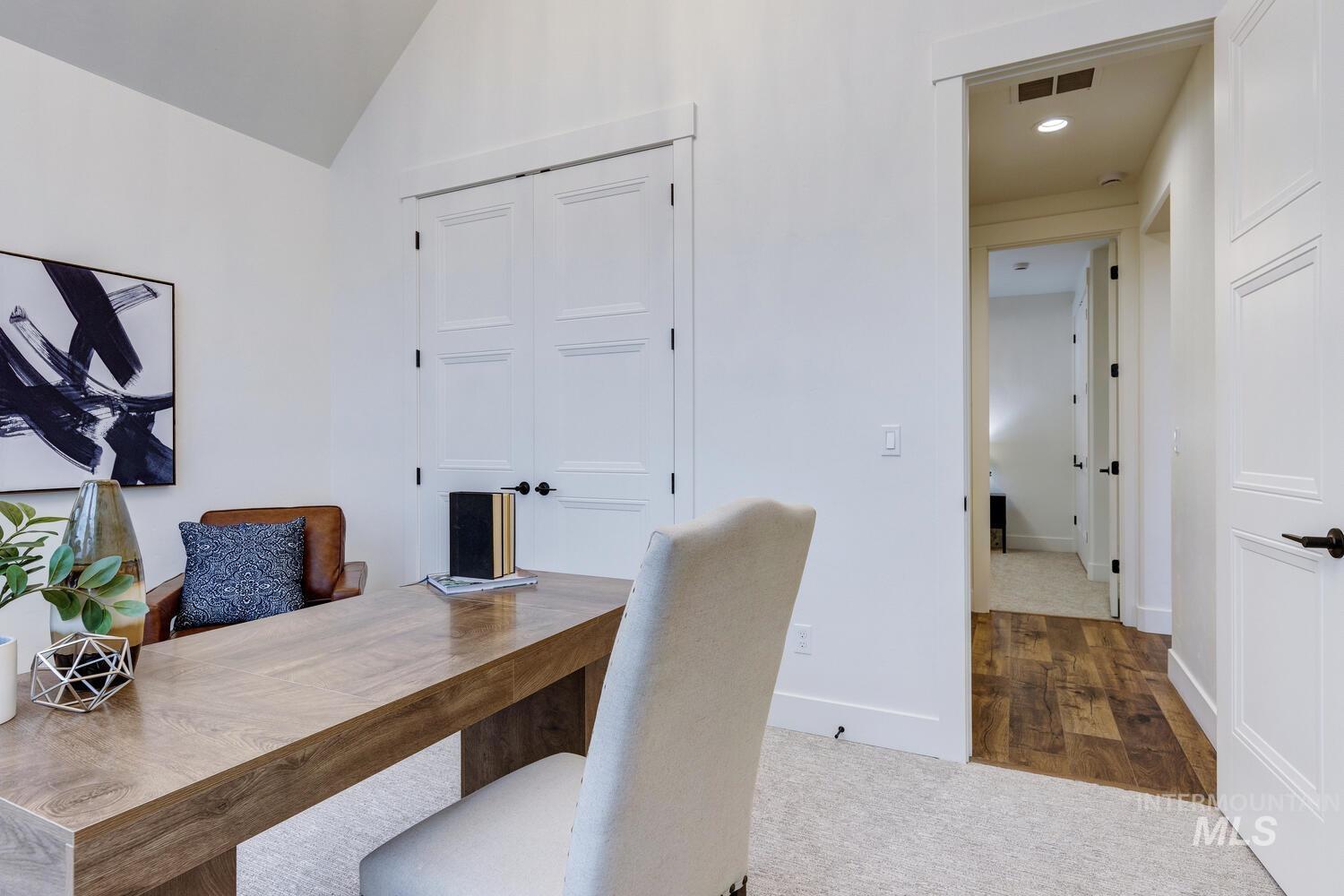 Carpeted home office with lofted ceiling and wood finished floors