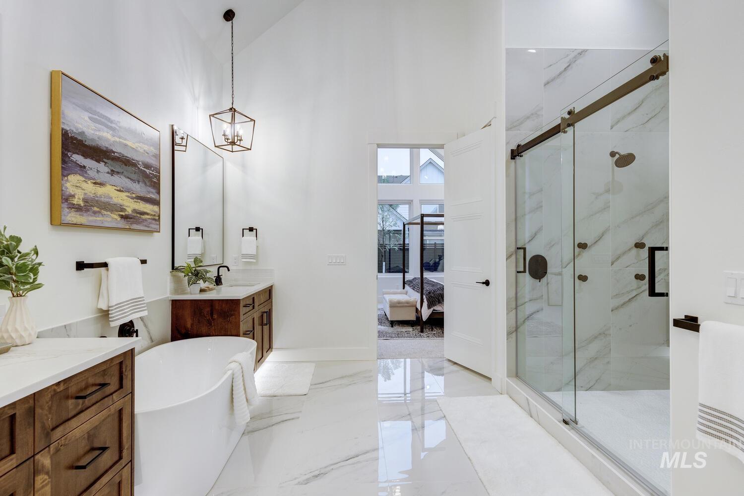 Full bath featuring light marble finish floors, vanity, a marble finish shower, a freestanding bath, and a high ceiling