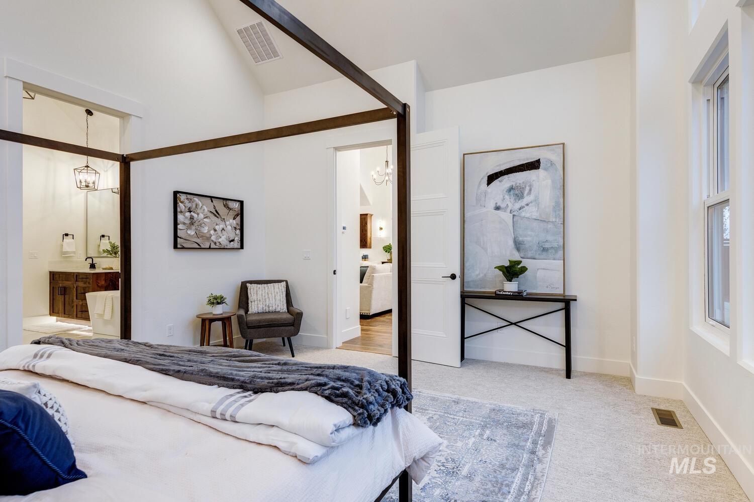 Carpeted bedroom with a chandelier, ensuite bathroom, and high vaulted ceiling
