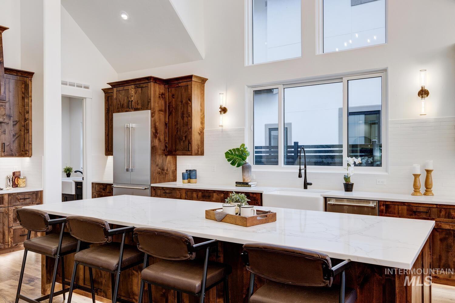Kitchen featuring decorative backsplash, light wood-style flooring, light stone counters, and high vaulted ceiling