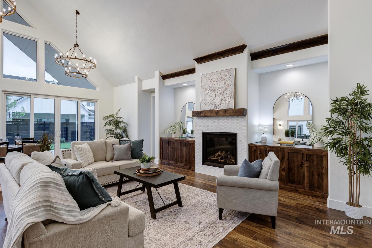Living room featuring high vaulted ceiling, a chandelier, dark wood-style flooring, and a glass covered fireplace