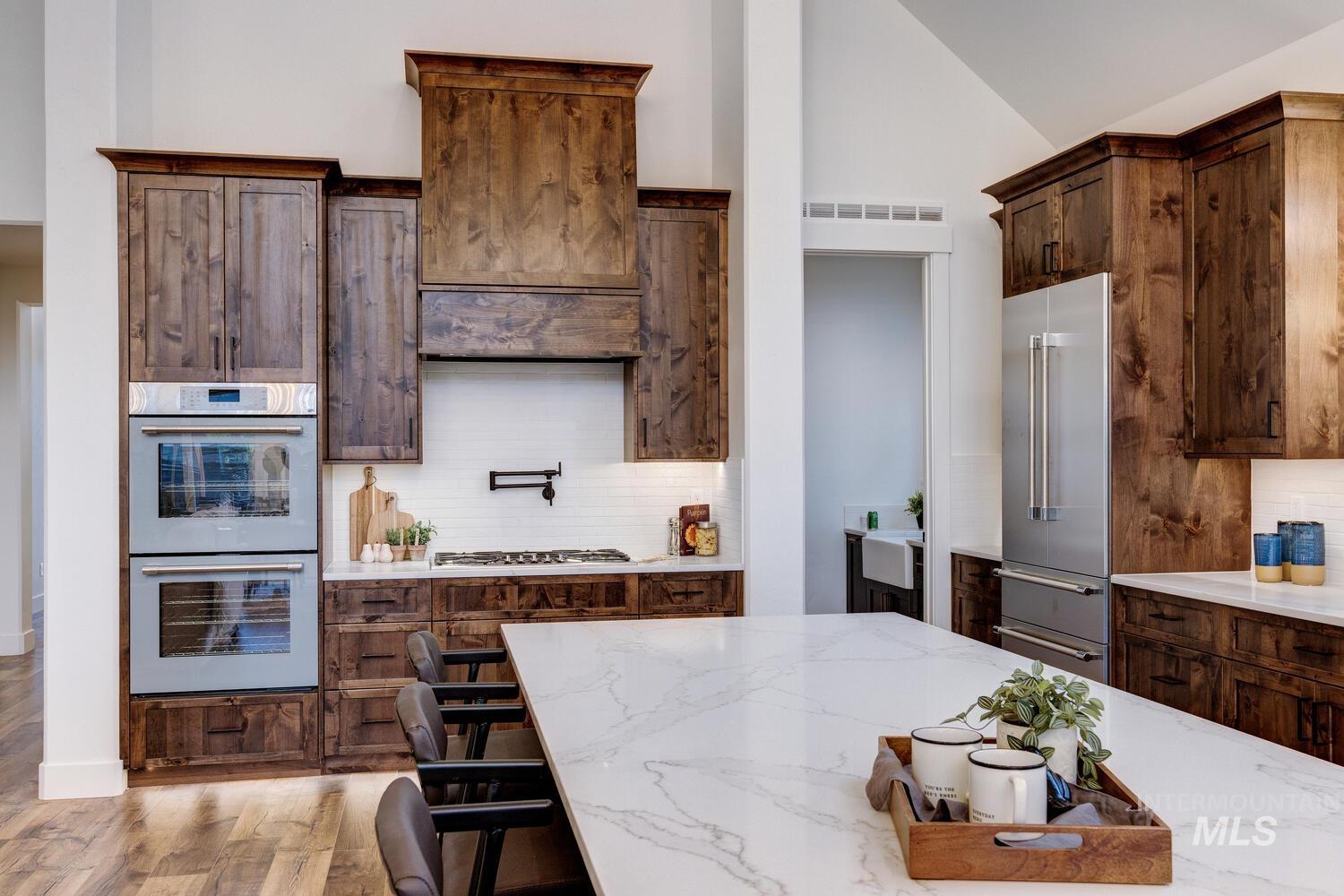 Kitchen with double wall oven, tasteful backsplash, light wood-type flooring, vaulted ceiling, and light stone counters