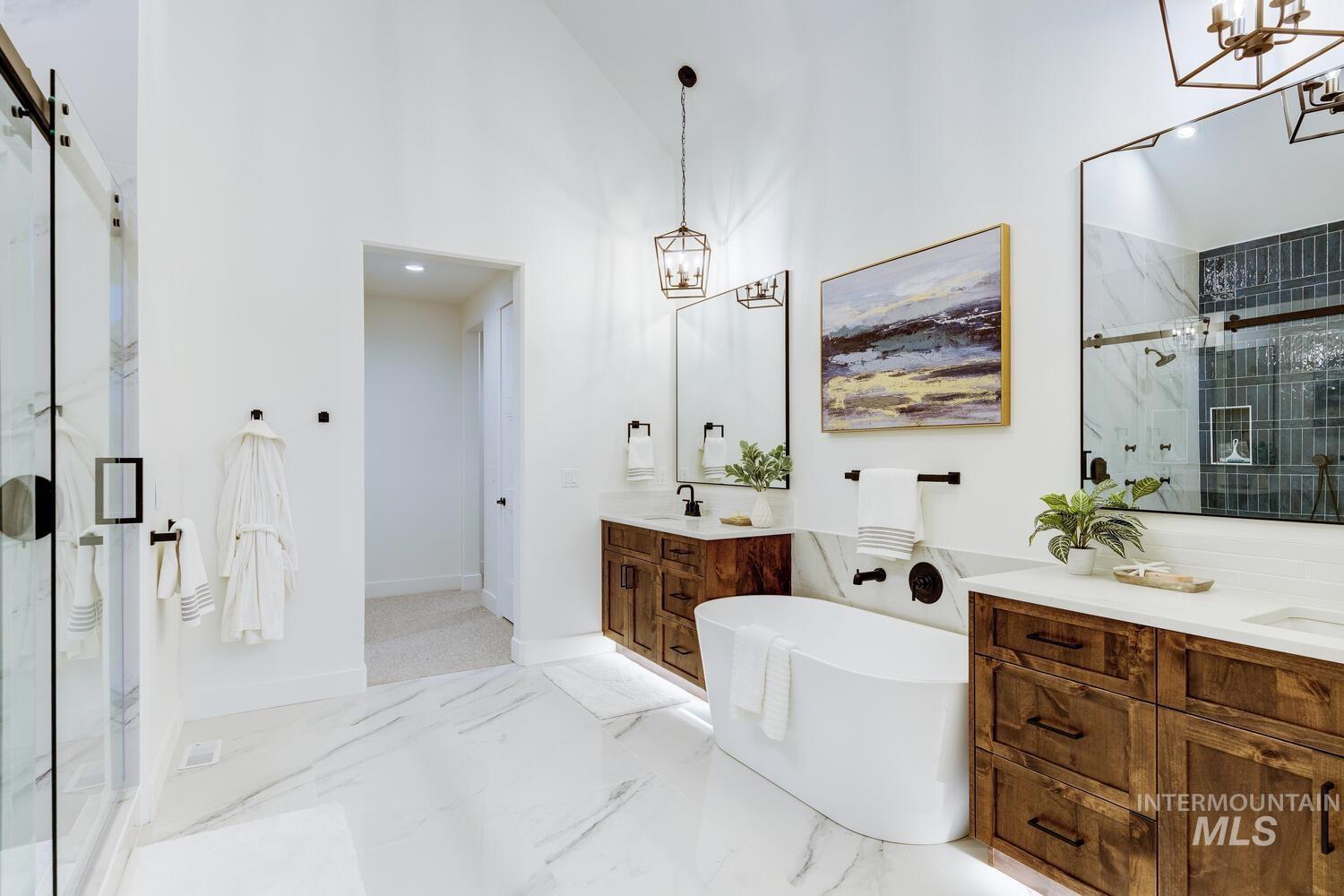 Bathroom with a chandelier, a marble finish shower, two vanities, a soaking tub, and light marble finish flooring