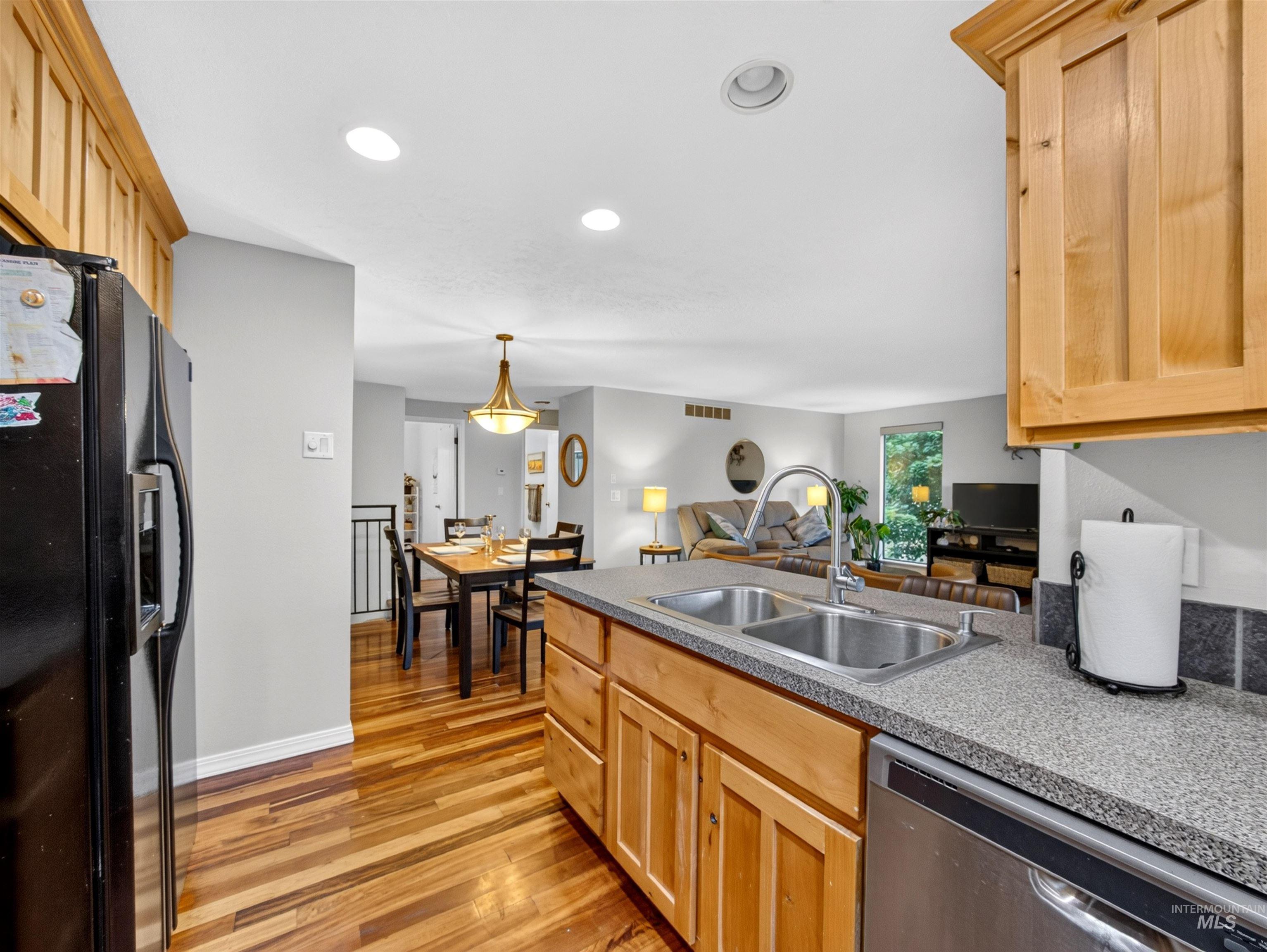 Kitchen featuring light wood cabinetry, a double basin stainless steel sink, a stainless steel dishwasher, and mottled gray countertops