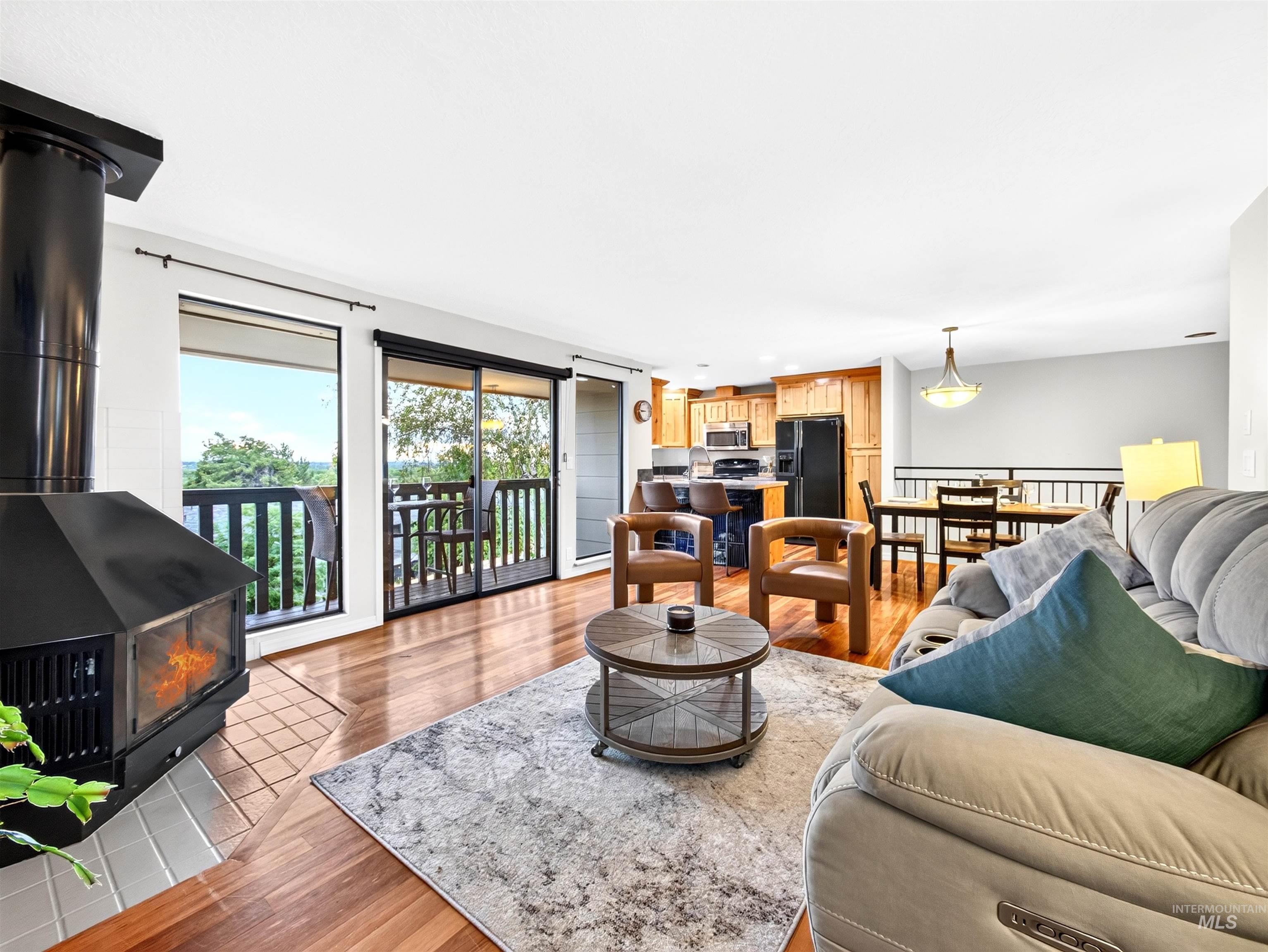 Living area with a freestanding black metal fireplace on a tiled hearth, wood-finish flooring, and a sliding glass door leading to a balcony