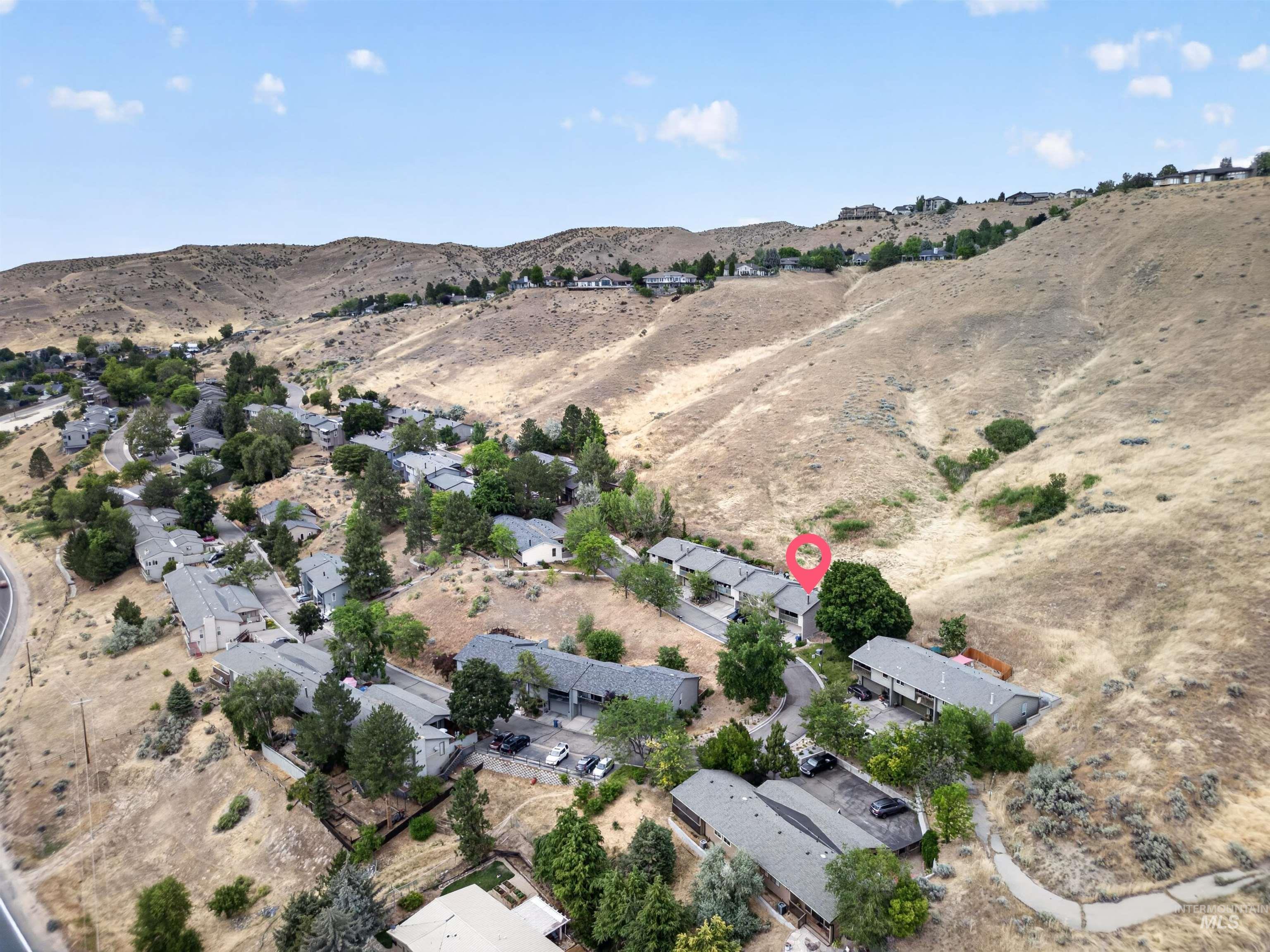 Hillside community featuring multiple residential structures with gray roofs, mature trees, and paved roadways
