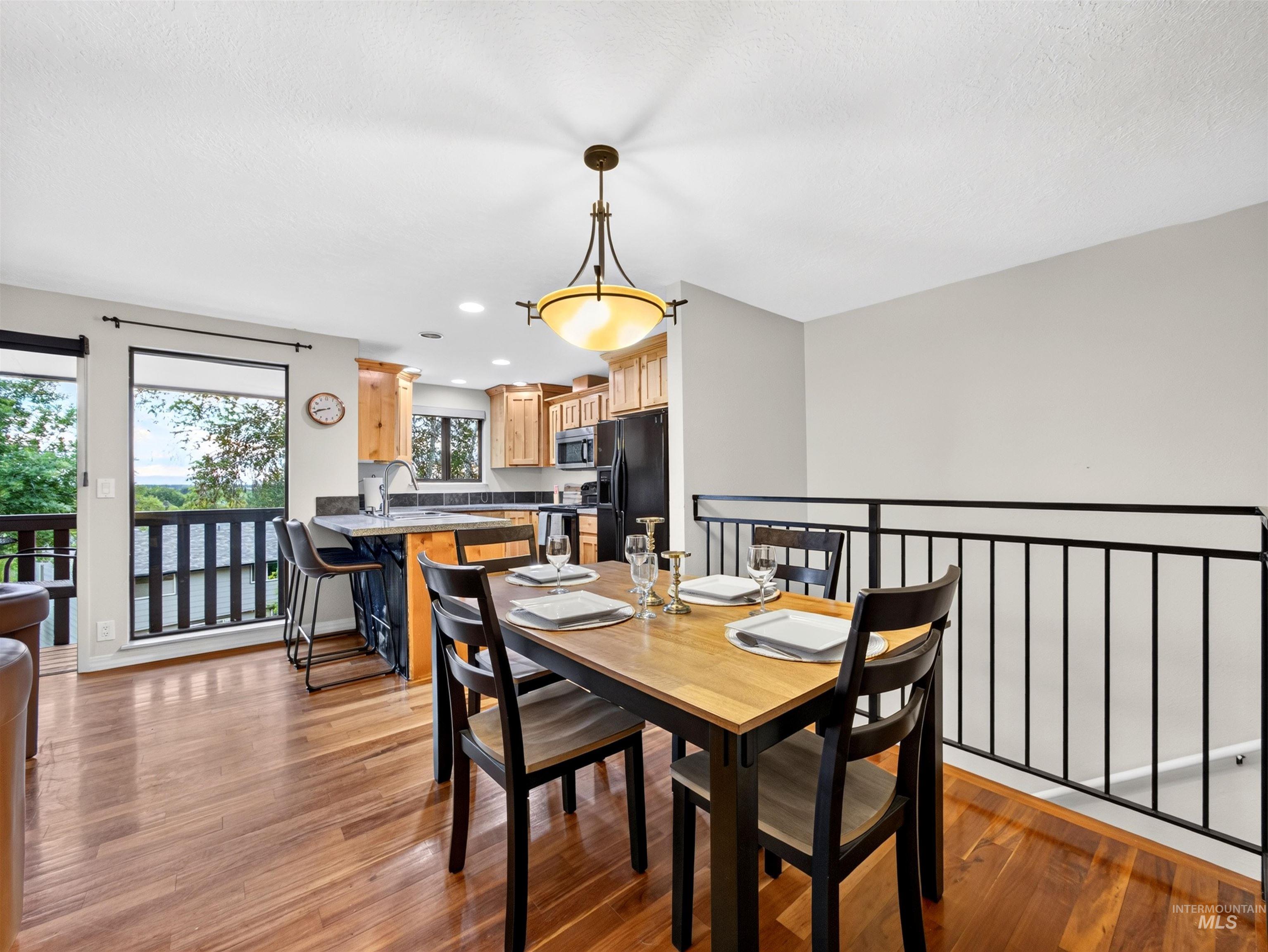 Open-concept dining area featuring wood-finish flooring, a contemporary chandelier, and a black metal railing