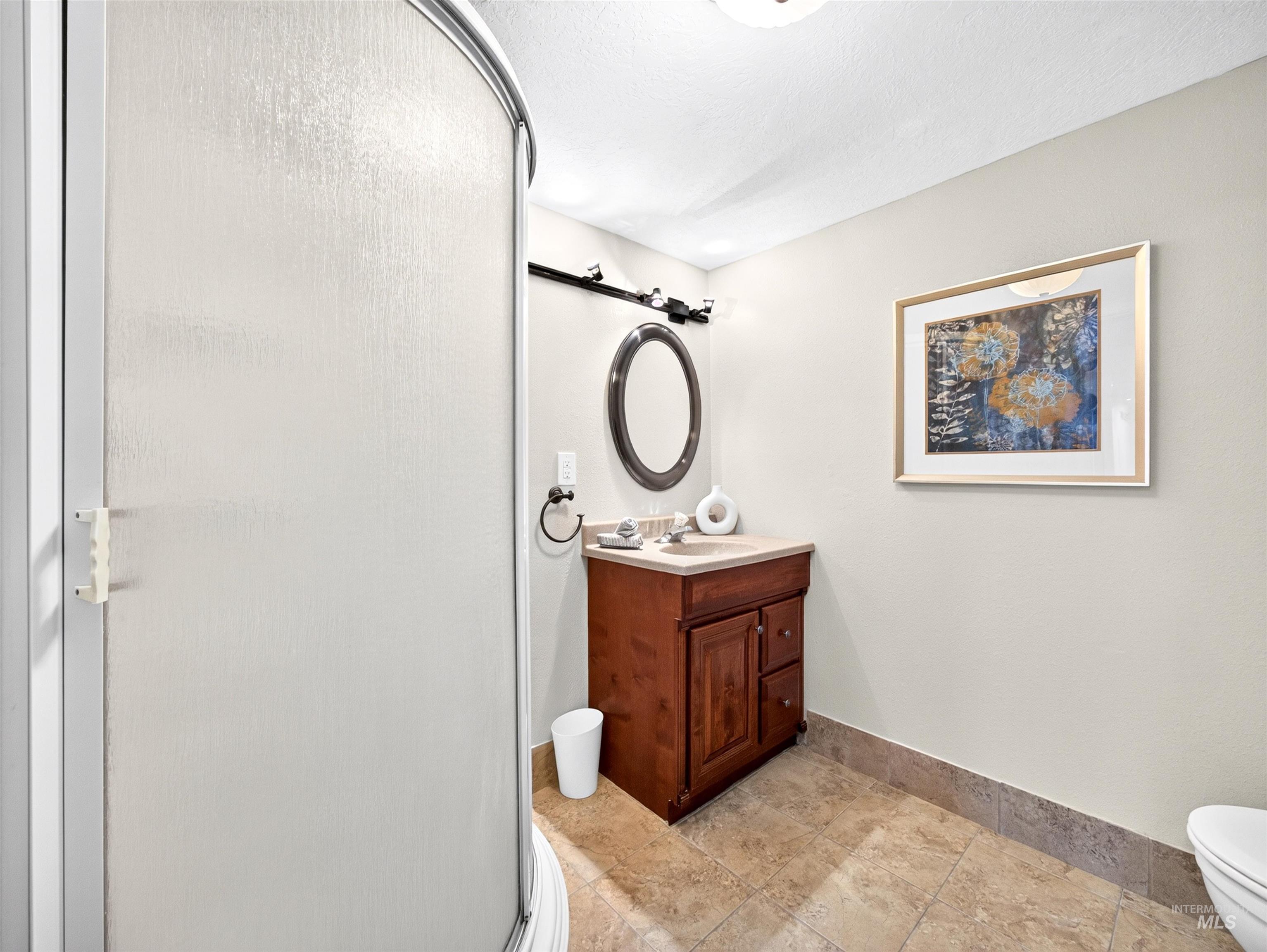 Bathroom featuring a frosted glass shower enclosure, wood-finish vanity with a countertop sink, and patterned tile flooring