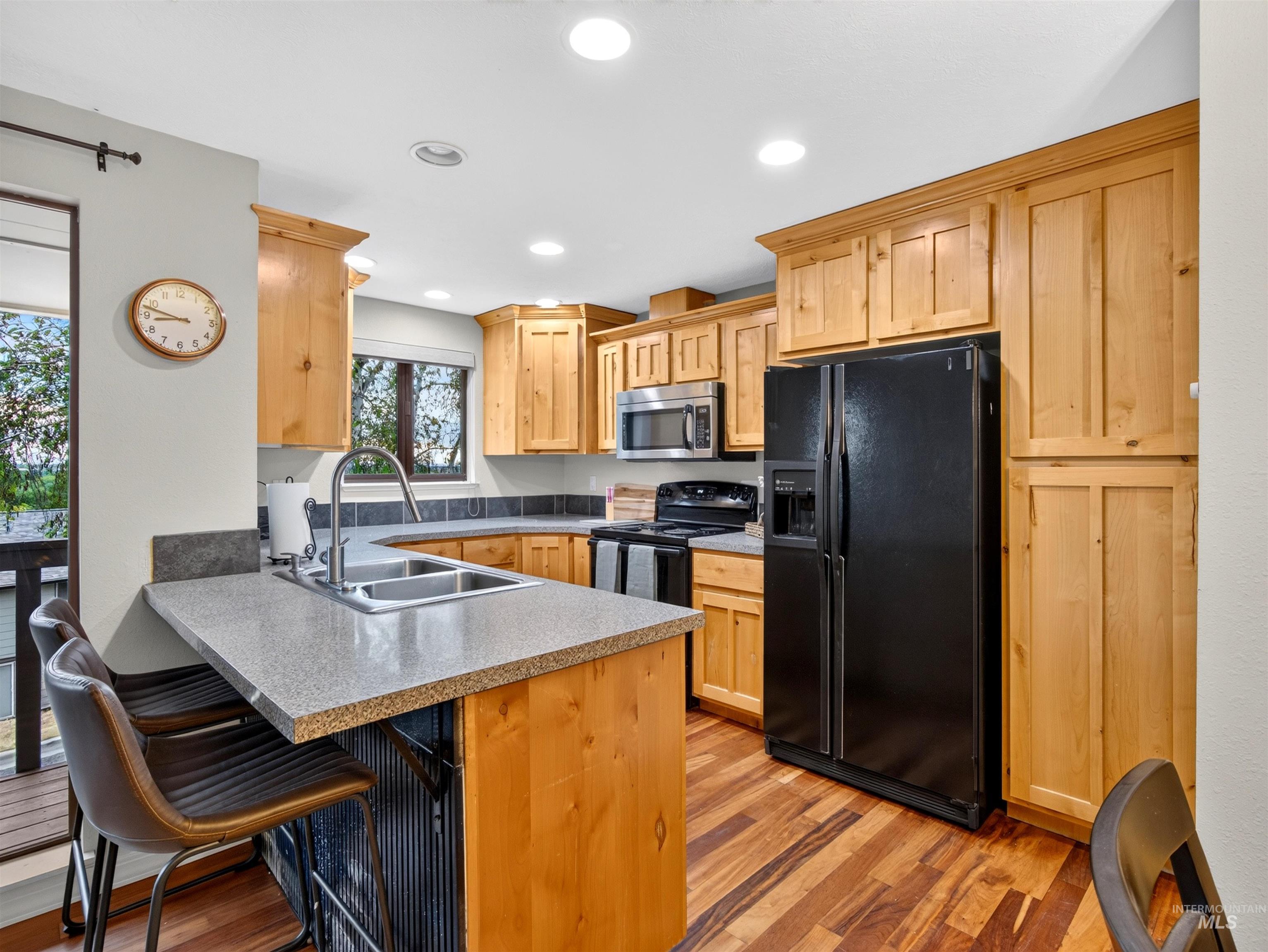 Kitchen featuring natural wood cabinetry, wood-finish flooring, a double basin stainless steel sink with a gooseneck faucet, black appliances, and recessed lighting