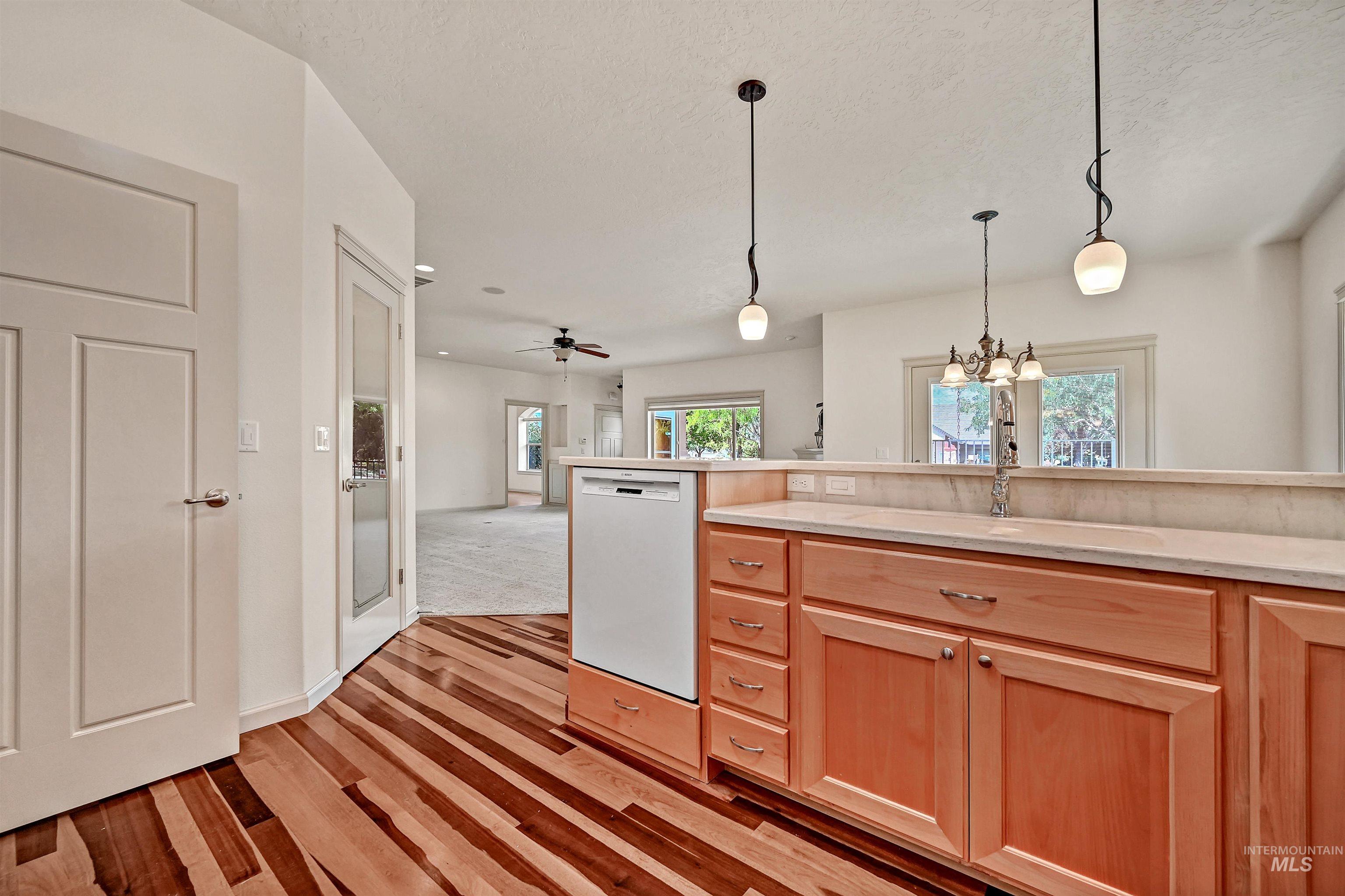 Kitchen featuring white dishwasher, hanging light fixtures, light brown cabinetry, open floor plan, and light wood finished floors