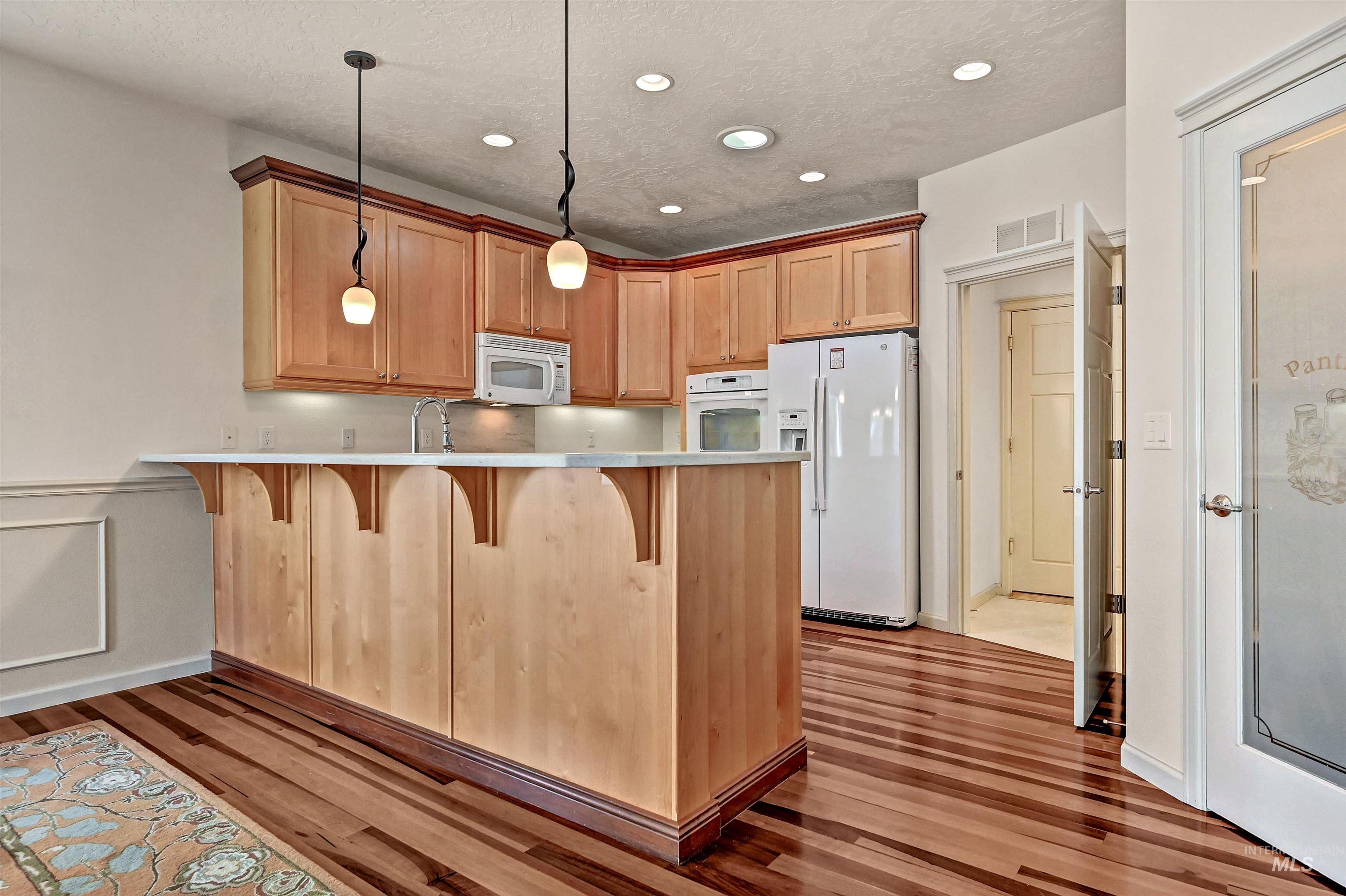 Kitchen featuring white appliances, a breakfast bar area, pendant lighting, a peninsula, and light wood-style floors