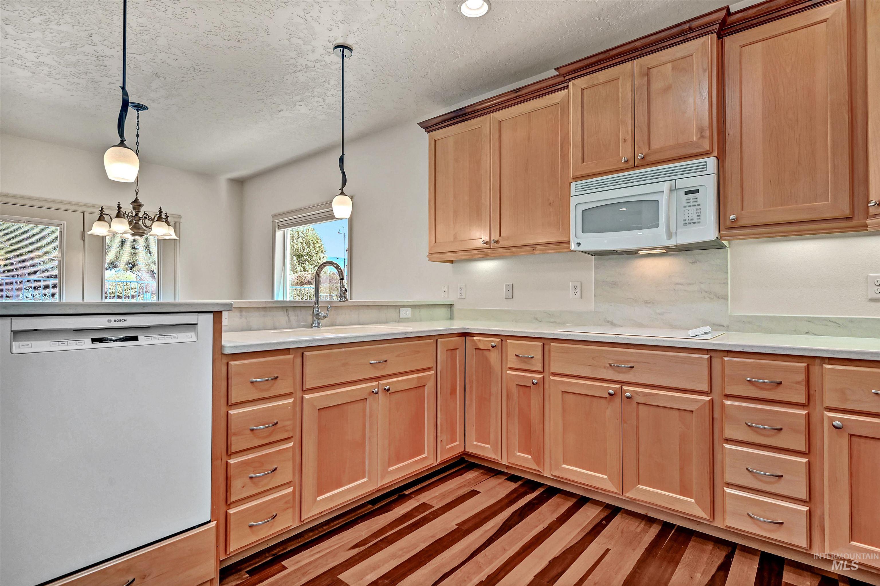 Kitchen with stainless steel dishwasher, white microwave, light countertops, a textured ceiling, and pendant lighting