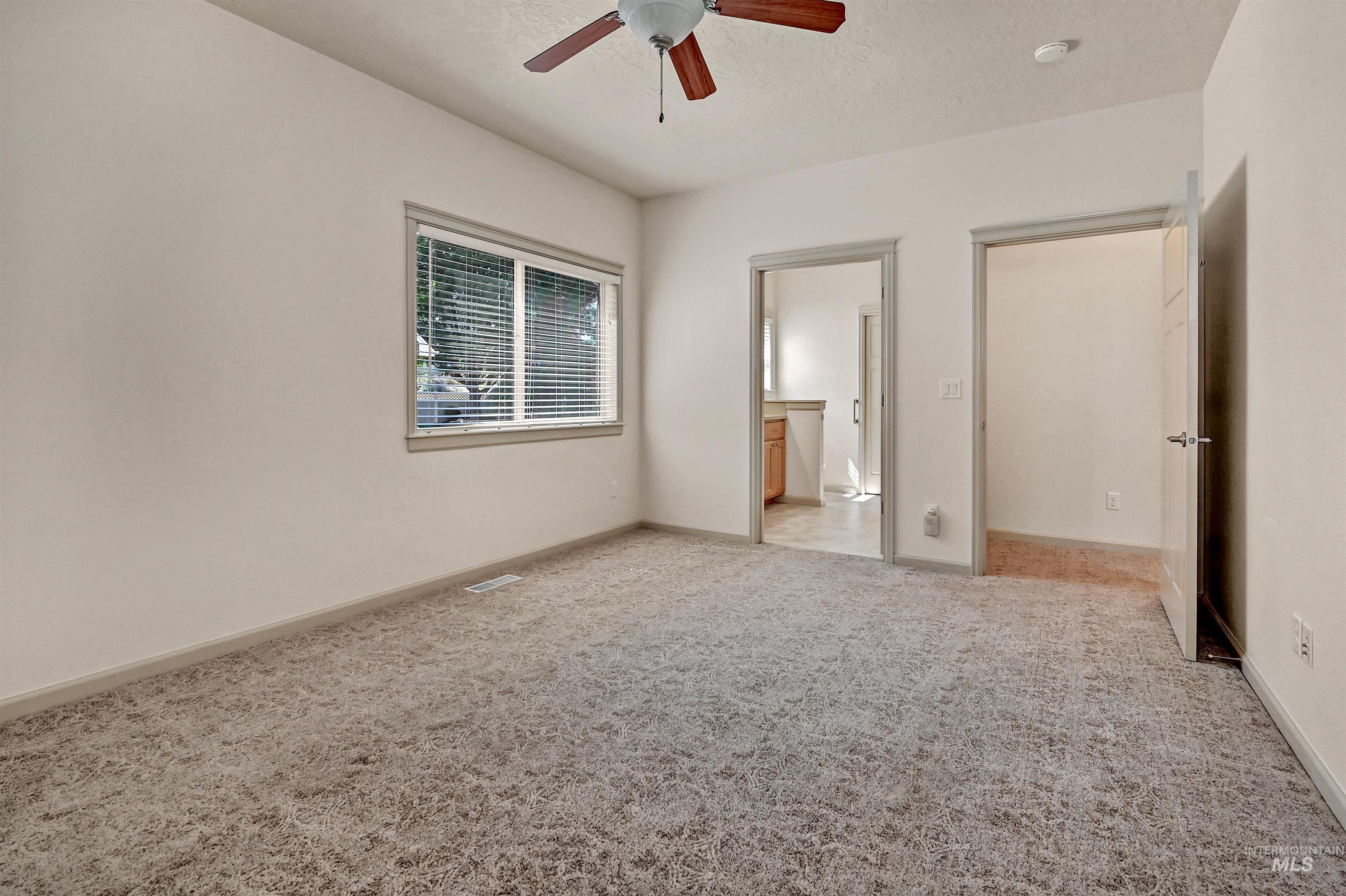 Unfurnished bedroom featuring light carpet, ensuite bathroom, a textured ceiling, and ceiling fan