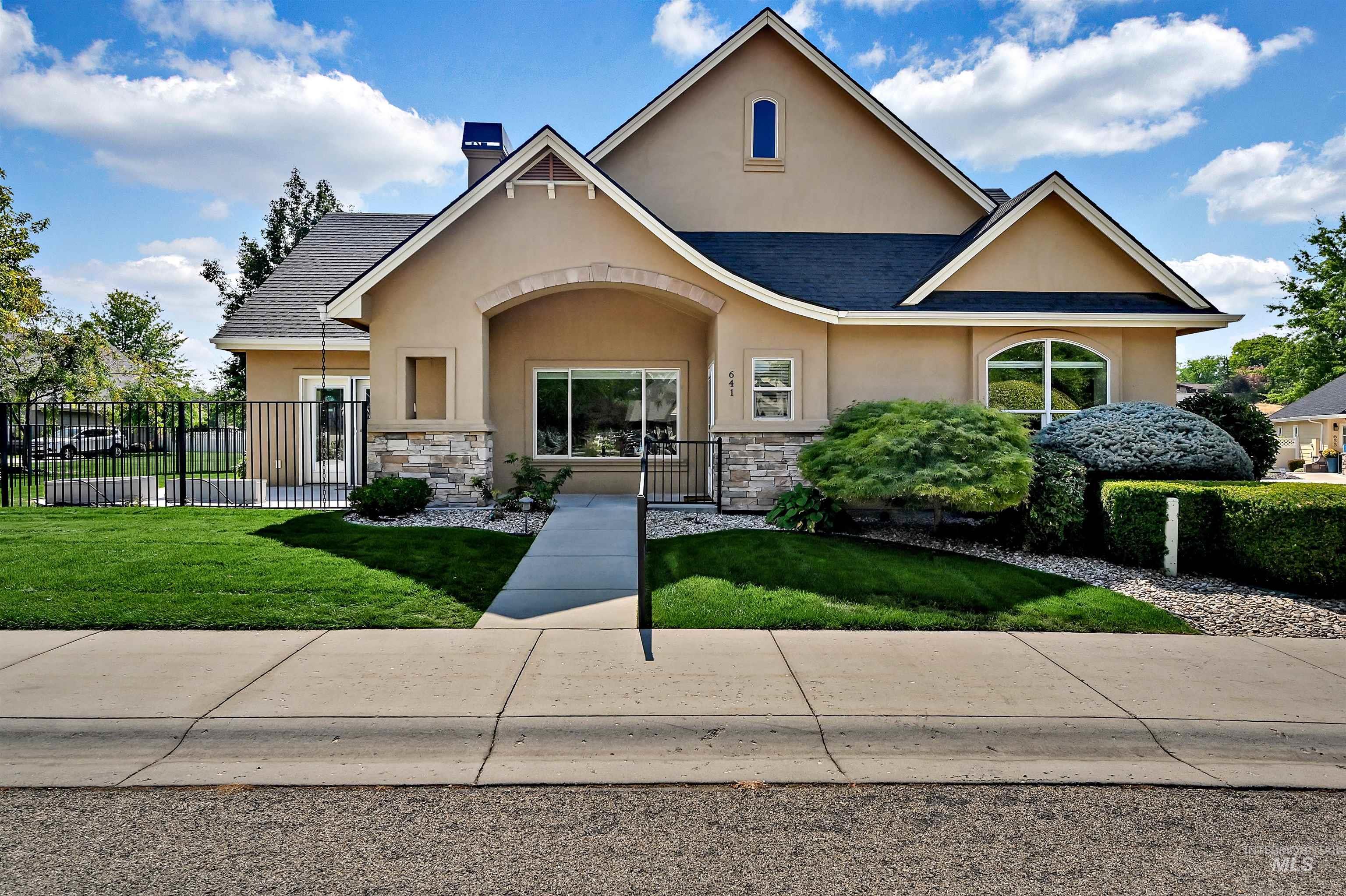 View of front of home with stucco siding, roof with shingles, a chimney, and stone siding