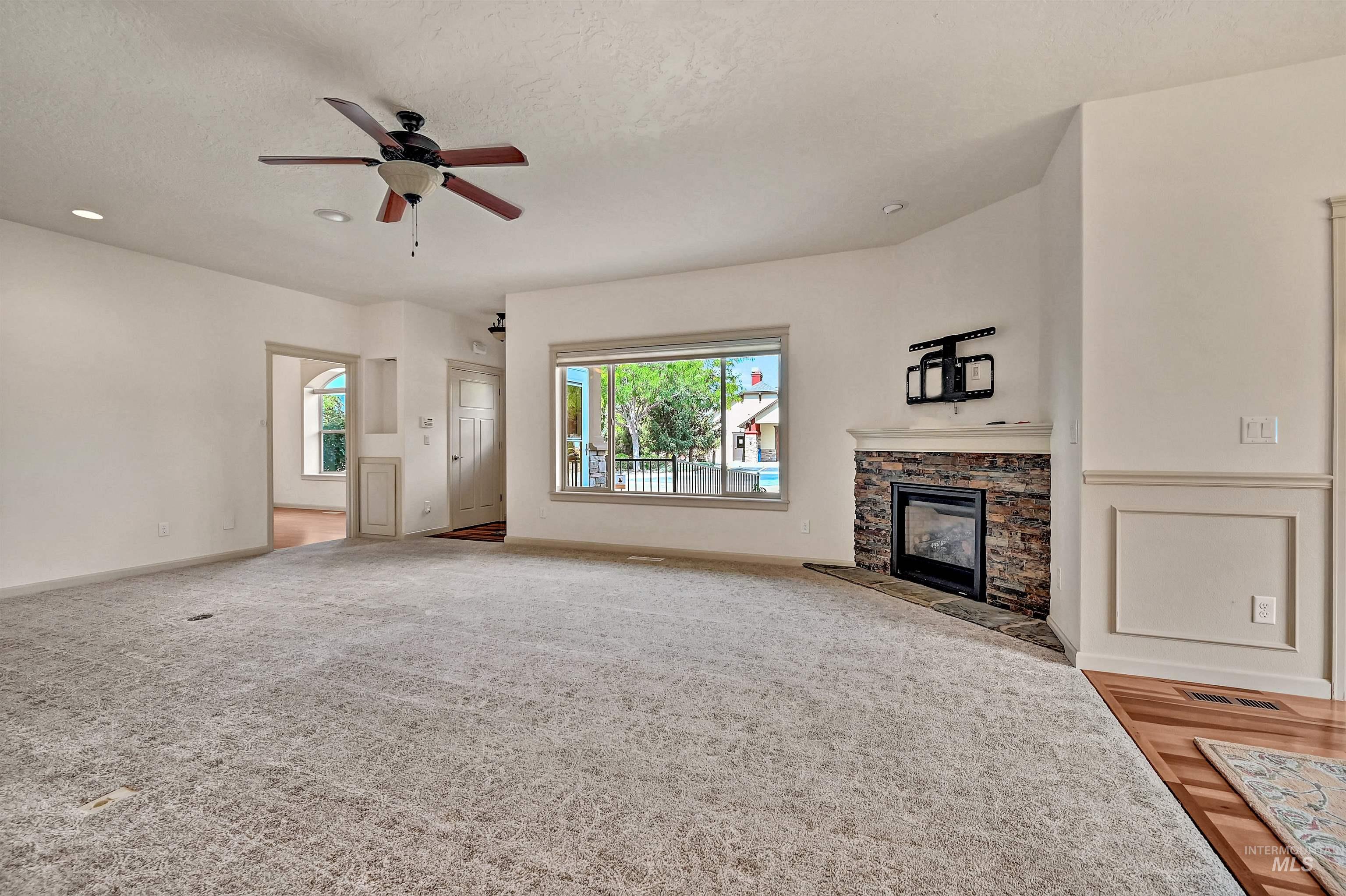 Unfurnished living room with a stone fireplace, ceiling fan, a textured ceiling, recessed lighting, and carpet
