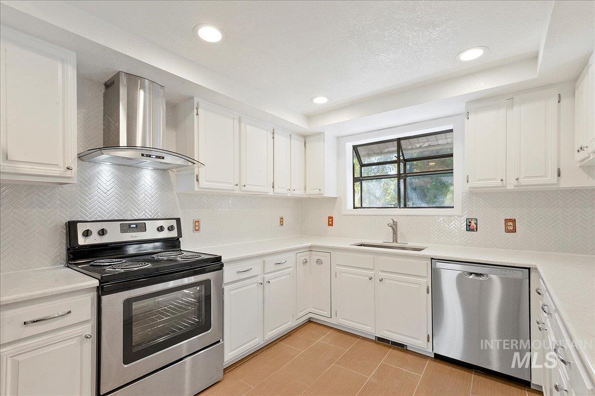 Kitchen featuring appliances with stainless steel finishes, backsplash, wall chimney range hood, white cabinets, and recessed lighting