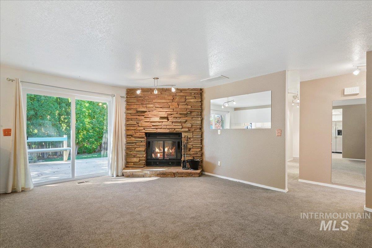 Unfurnished living room featuring a stone fireplace, carpet flooring, and a textured ceiling
