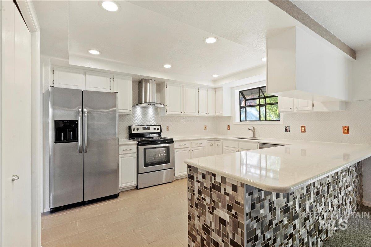 Kitchen featuring stainless steel appliances, decorative backsplash, recessed lighting, wall chimney range hood, and a peninsula