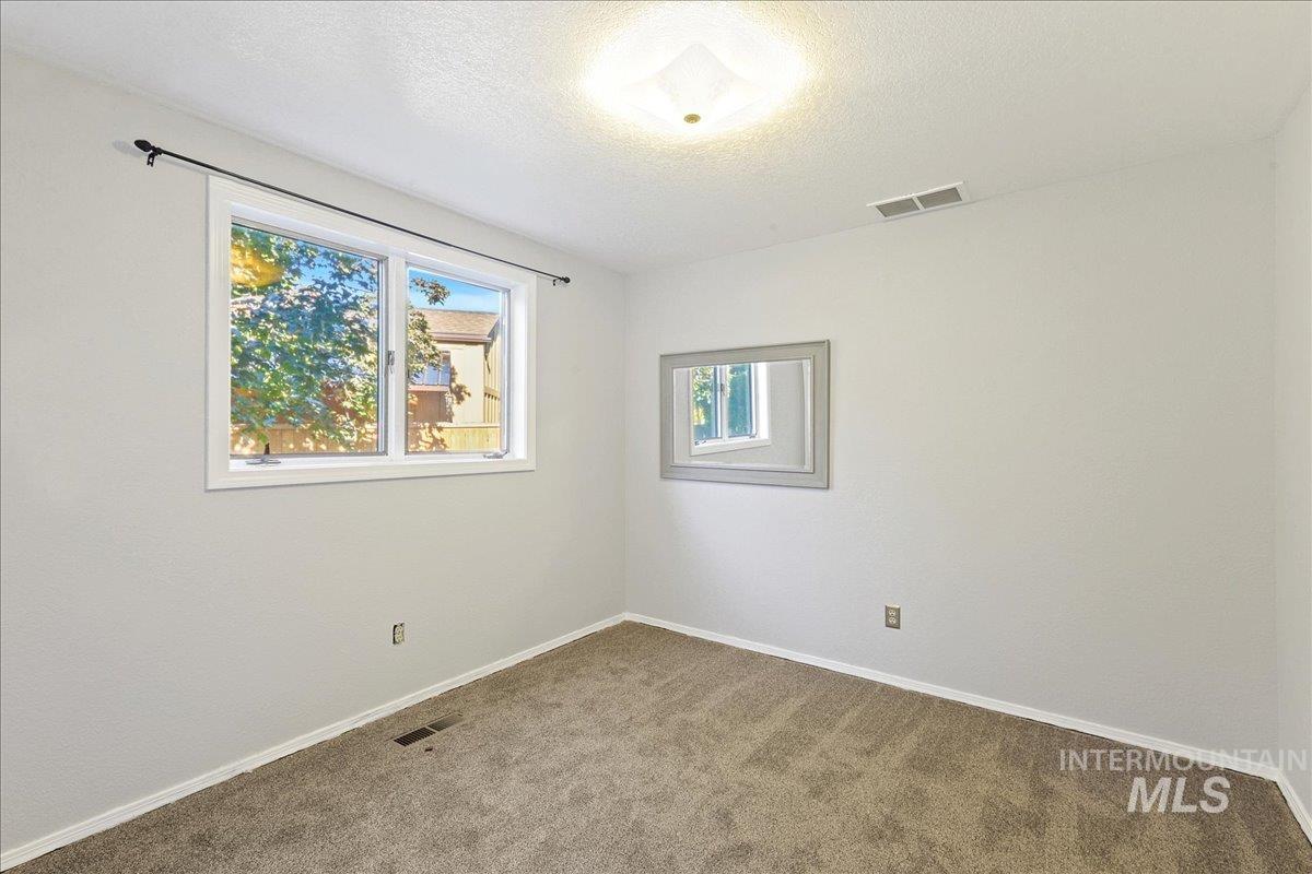 Carpeted empty room with a textured ceiling and baseboards