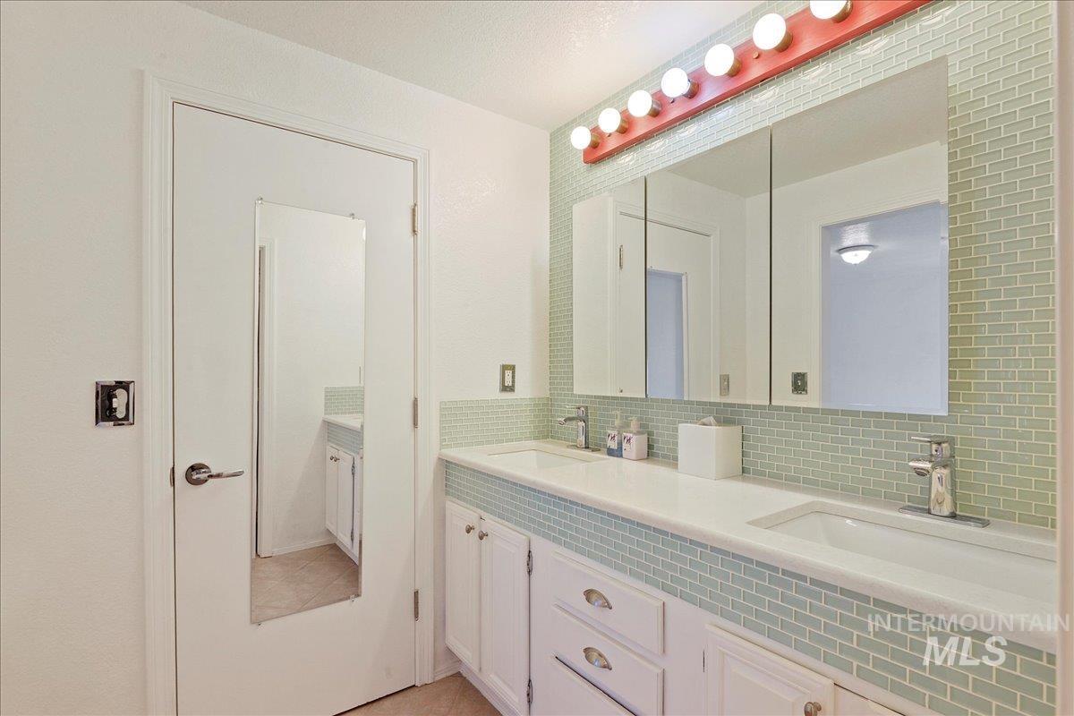 Full bath with double vanity, tasteful backsplash, and light tile patterned floors