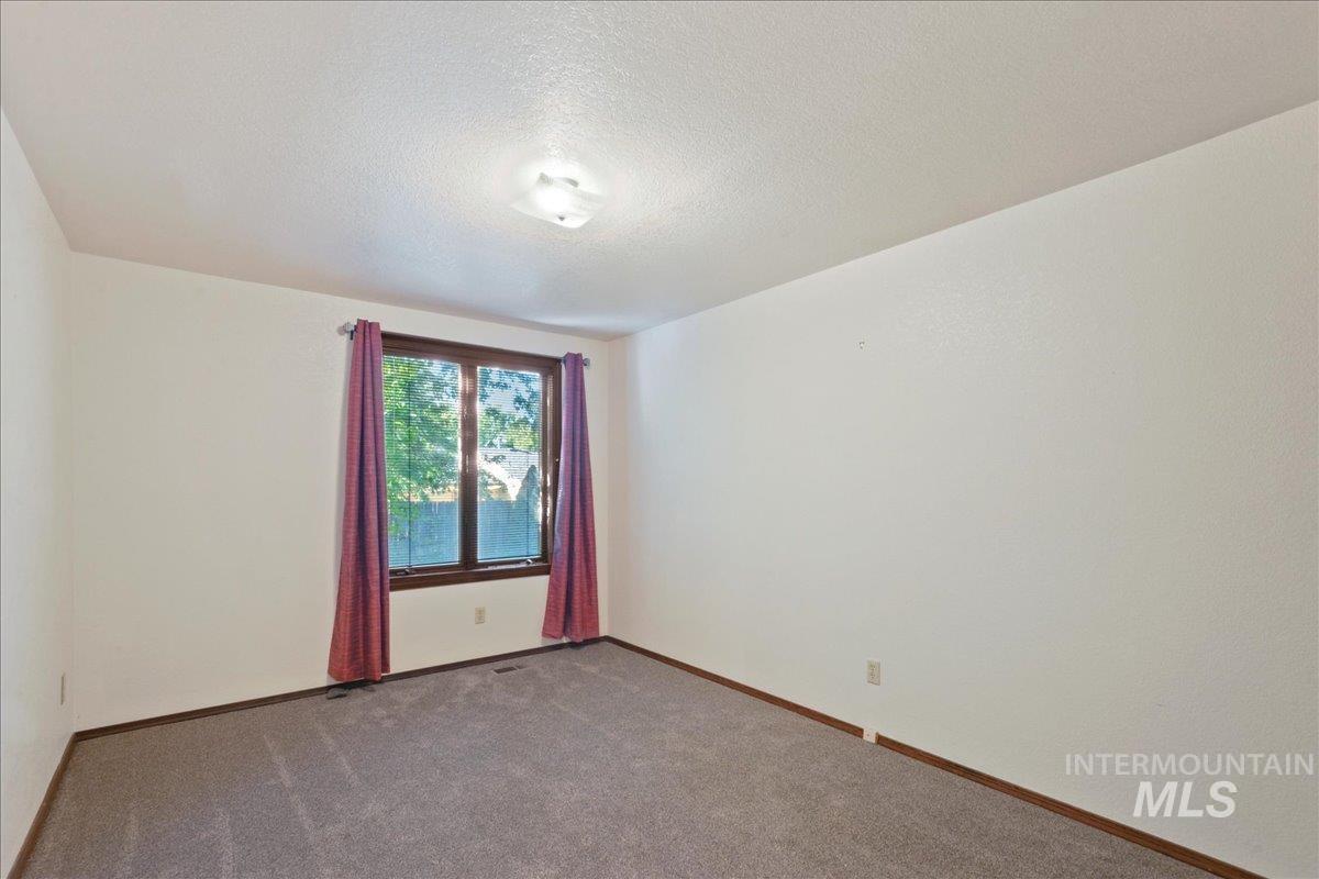 Carpeted spare room featuring a textured ceiling and baseboards
