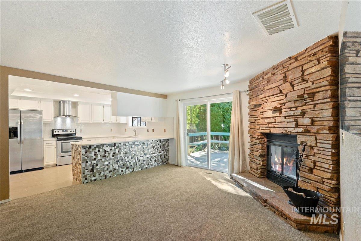Unfurnished living room featuring a textured ceiling, light colored carpet, a fireplace, and track lighting