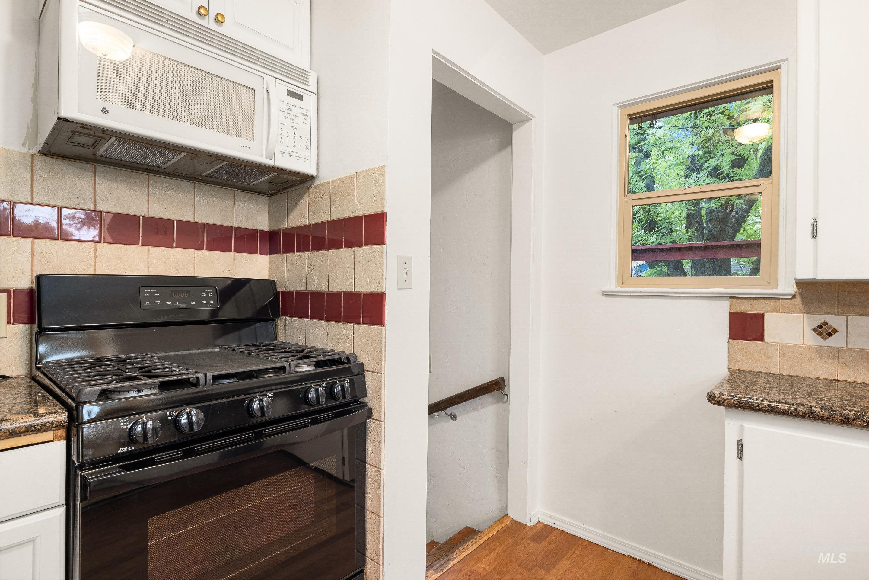 Kitchen featuring tasteful backsplash, black gas stove, white cabinetry, white microwave, and light wood-style floors